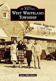 Four people standing in front of a building with signs for West Whiteland Township and a dairy grille restaurant. There is an animal (likely a goat) on top of the restaurant sign.