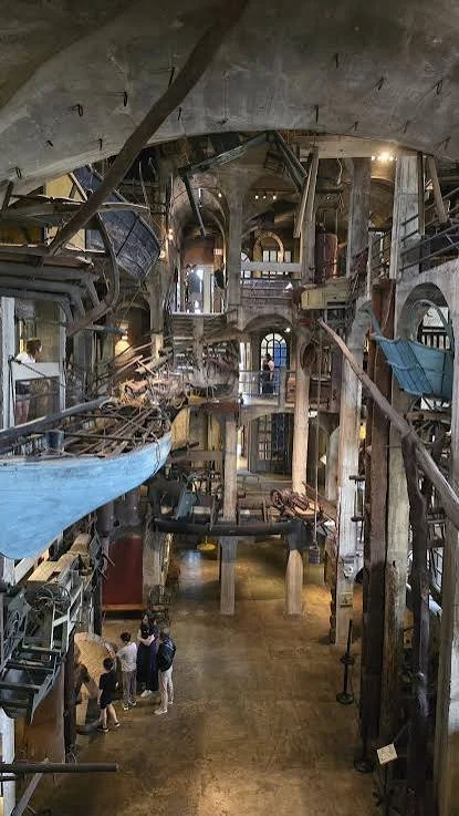 Interior of the Nautilus submarine exhibit with boats, wooden beams, and visitors exploring.
