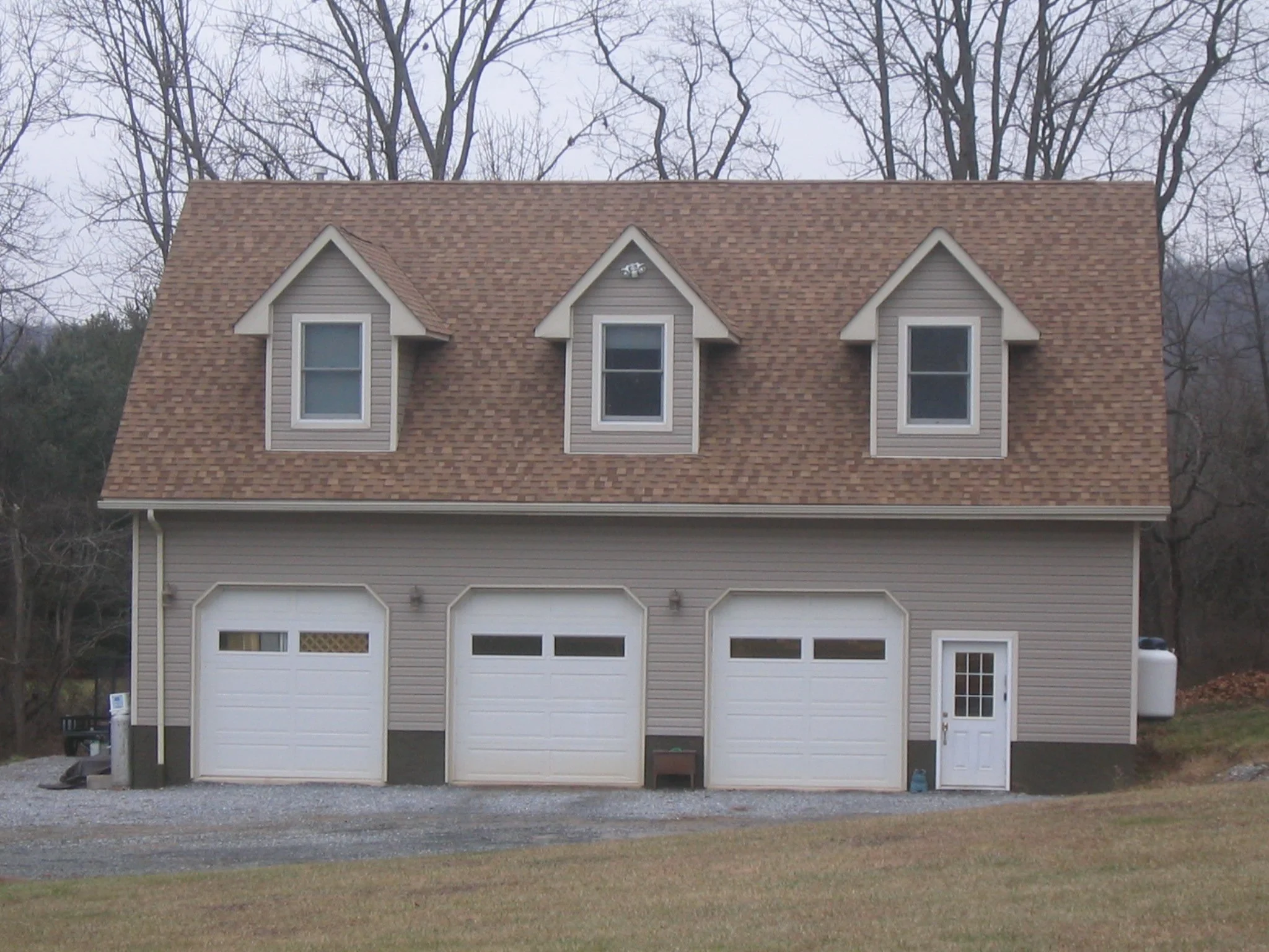 Front view of a two-story house with multiple roof gables, vinyl siding, three dormer windows, a garage with two doors, and a side door.