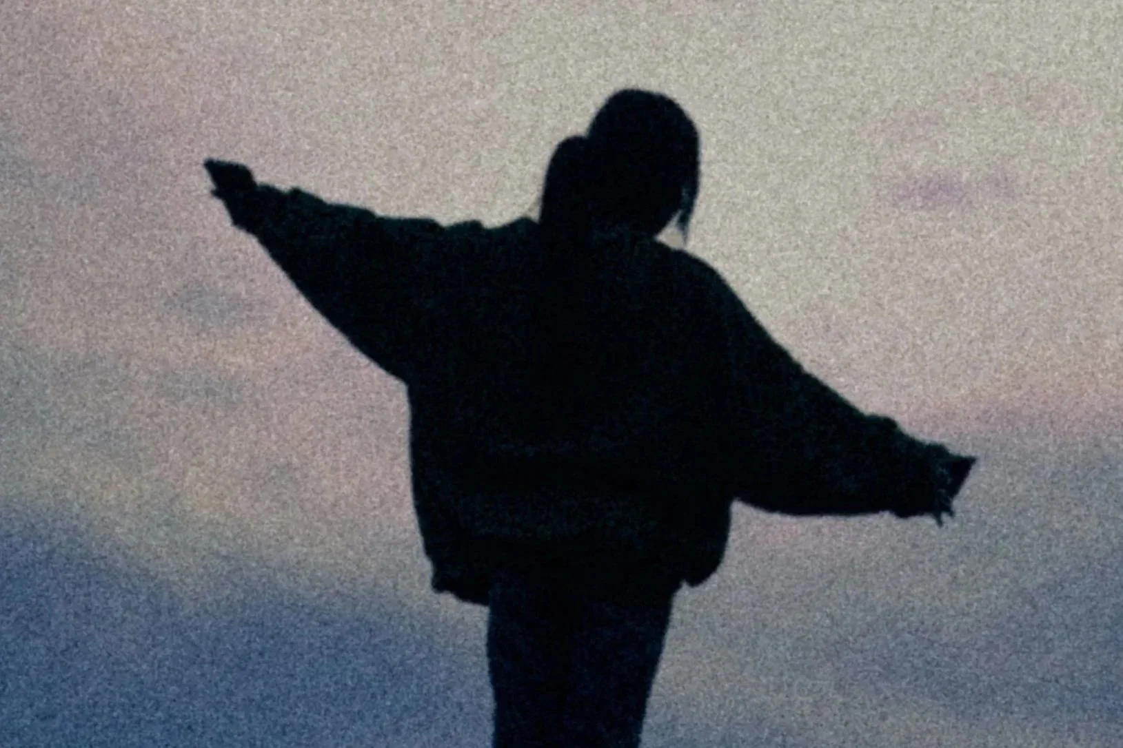 Silhouette of a person with arms outstretched against a gradient sky during sunset or sunrise