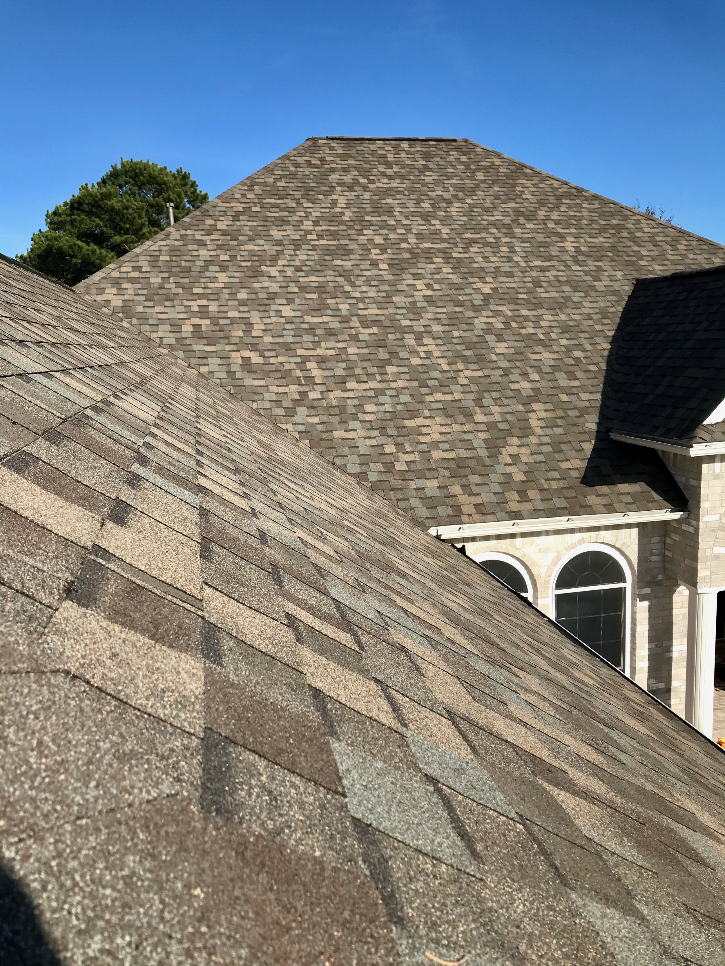 Multiple rooftops with different shingle styles and a clear blue sky in the background.
