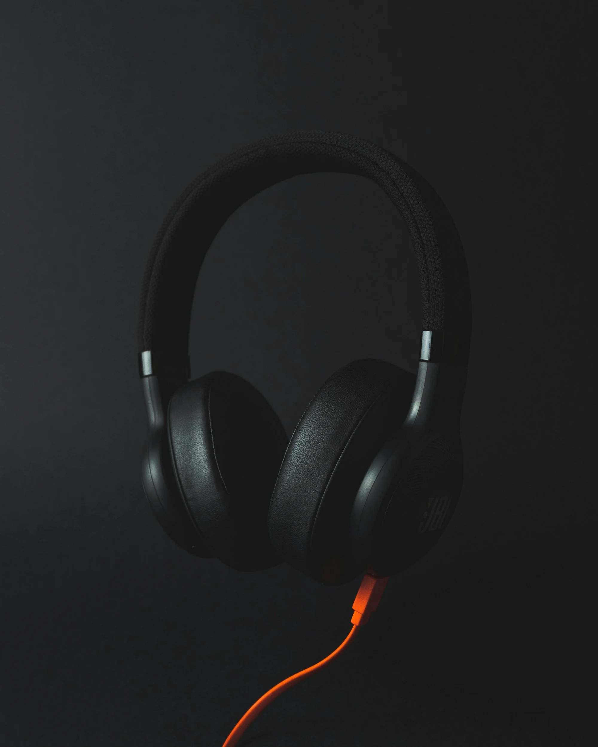 Close-up of black over-ear headphones connected to an orange audio cable, with a dark background.