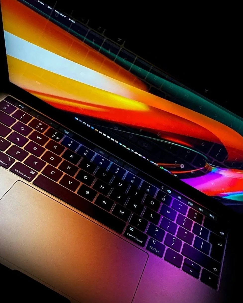 Close-up of an Apple MacBook with a colorful display and backlit keyboard showing purple, blue, and orange hues.