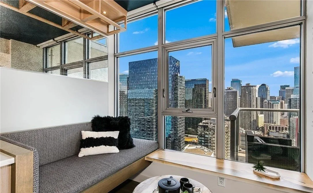 Interior of a high-rise apartment with a large window view of a city skyline, featuring modern furniture and decor.