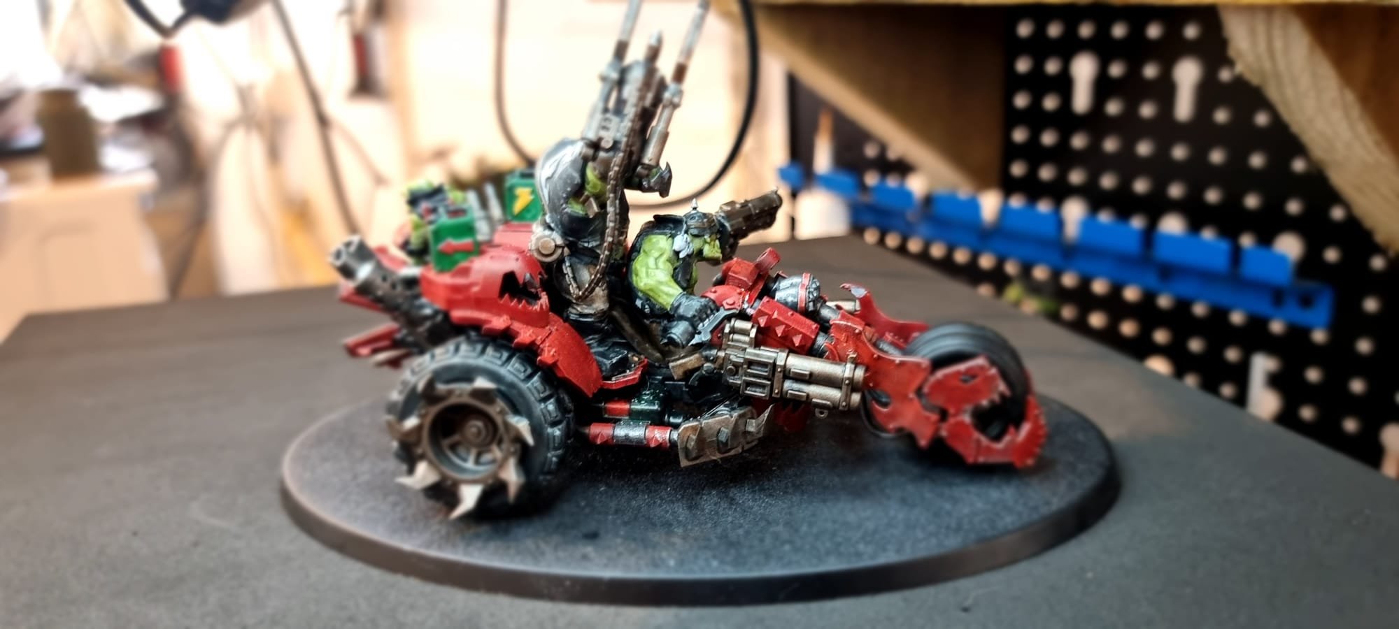 A detailed miniature model of a futuristic motorcycle with a green character seated on it, displayed on a black surface with a blurred background.