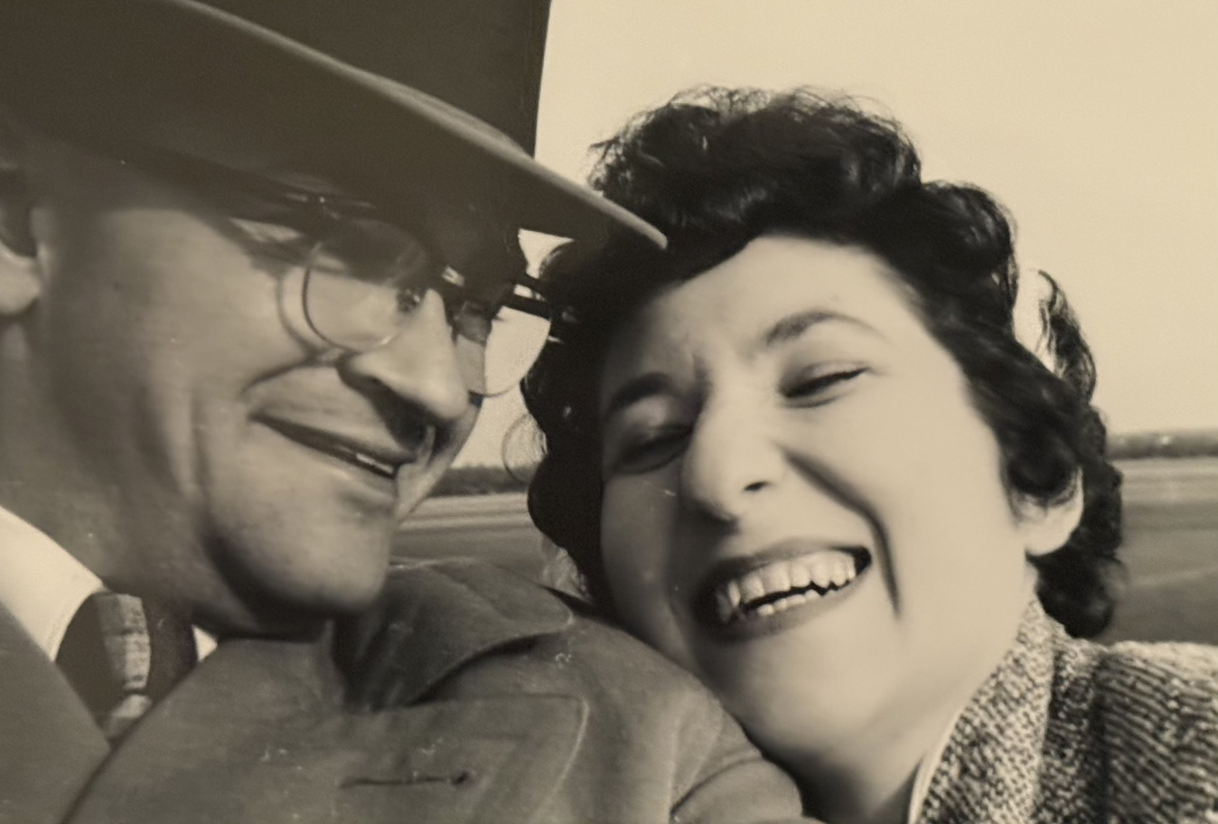 Black and white photo of a man and woman smiling, close-up shot with blurry background.