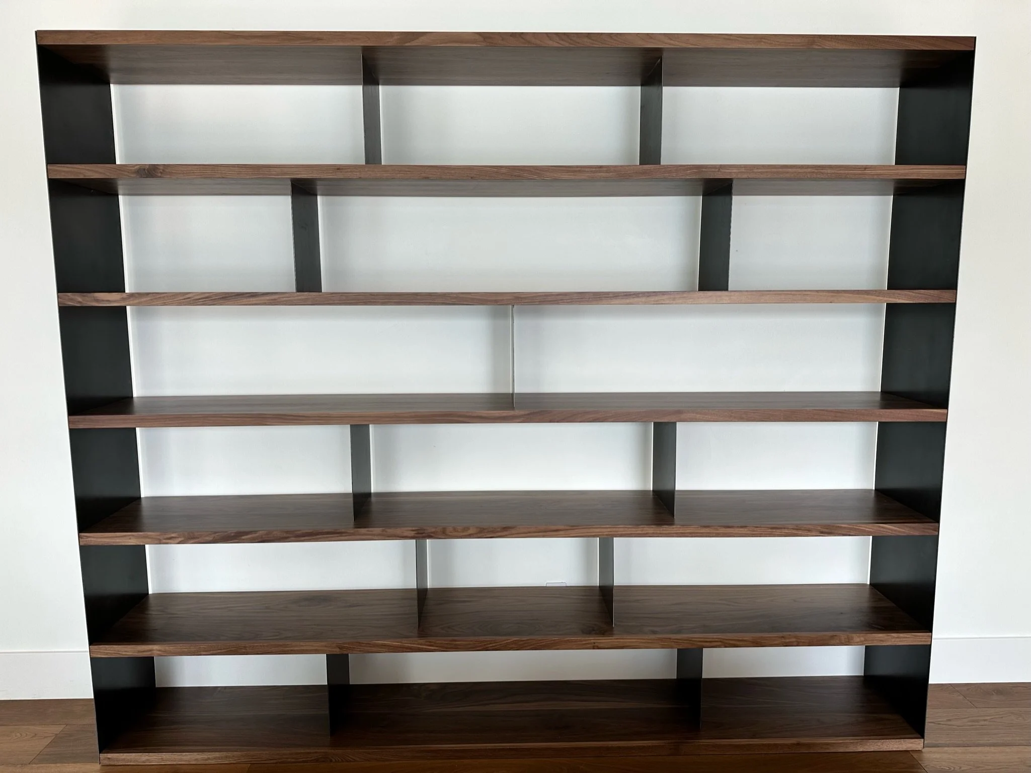 A two-tone wooden bookshelf with five shelves, featuring darker wood on the top and bottom and lighter wood on the middle shelves, against a plain wall.