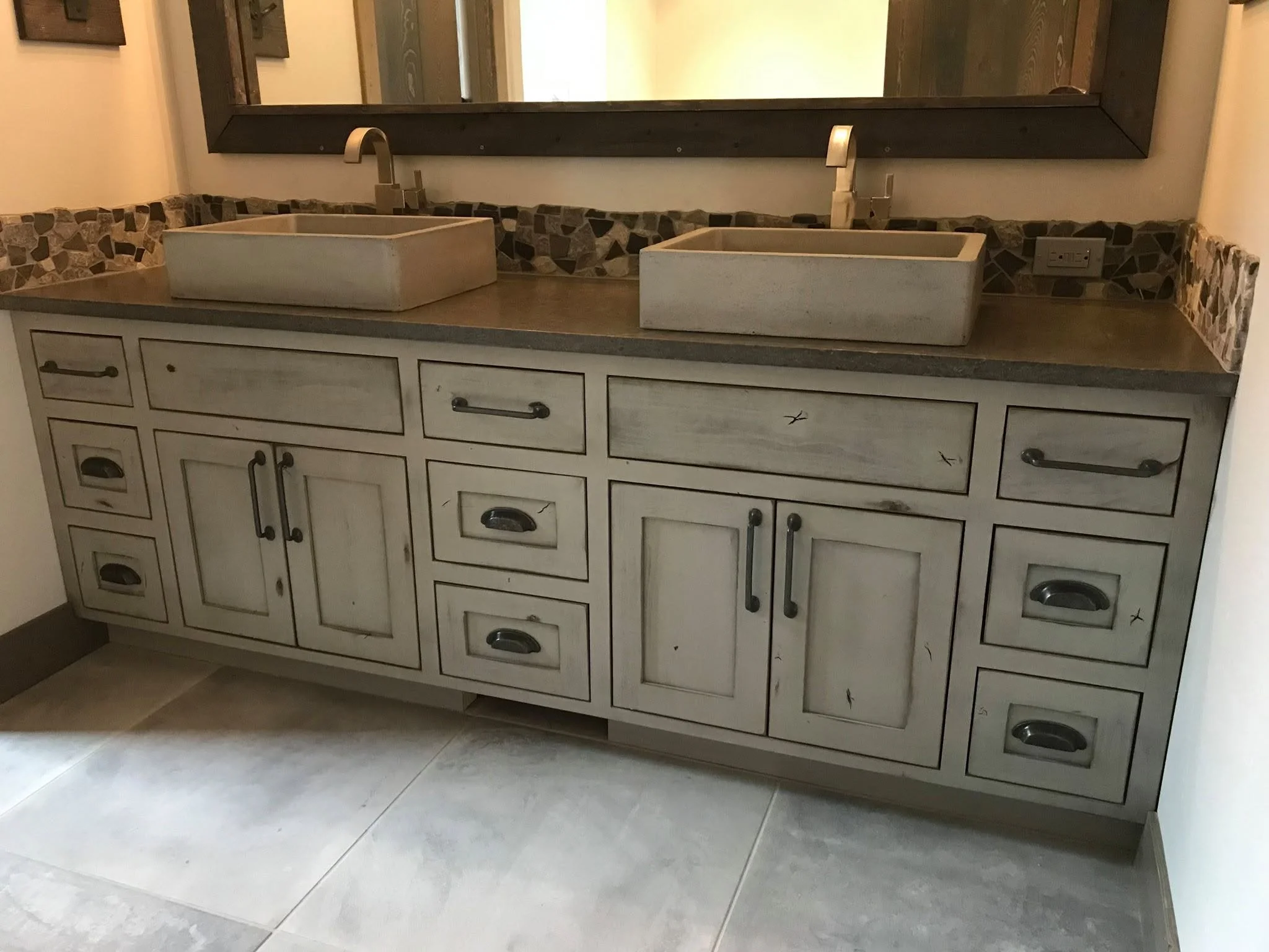 Double bathroom vanity with two rectangular vessel sinks, a large mirror, backsplash with stone tiles, and drawers and cabinets below.