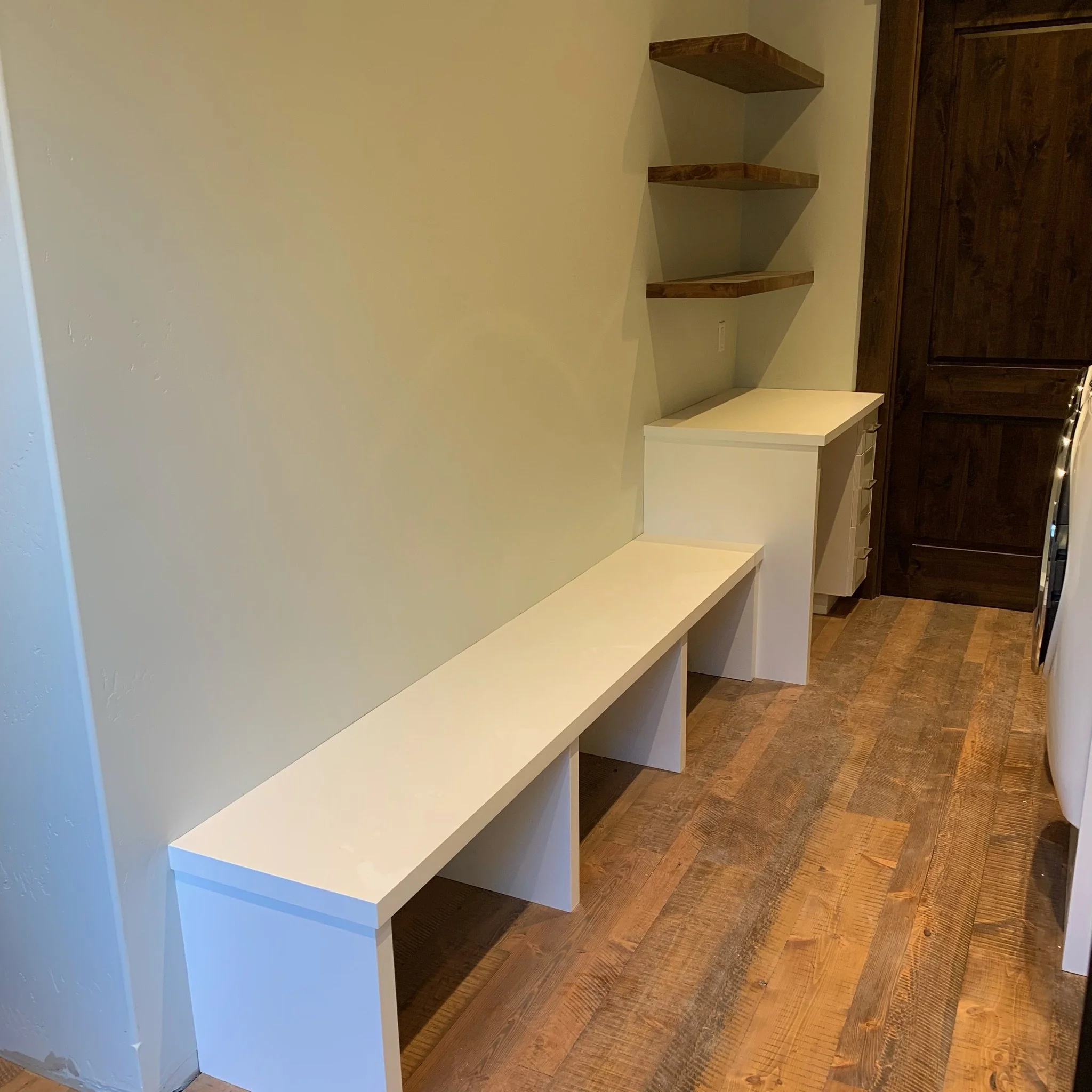 Built-in wooden shelves and a closed wooden cabinet in a corner of a room with a wooden floor and beige wall.