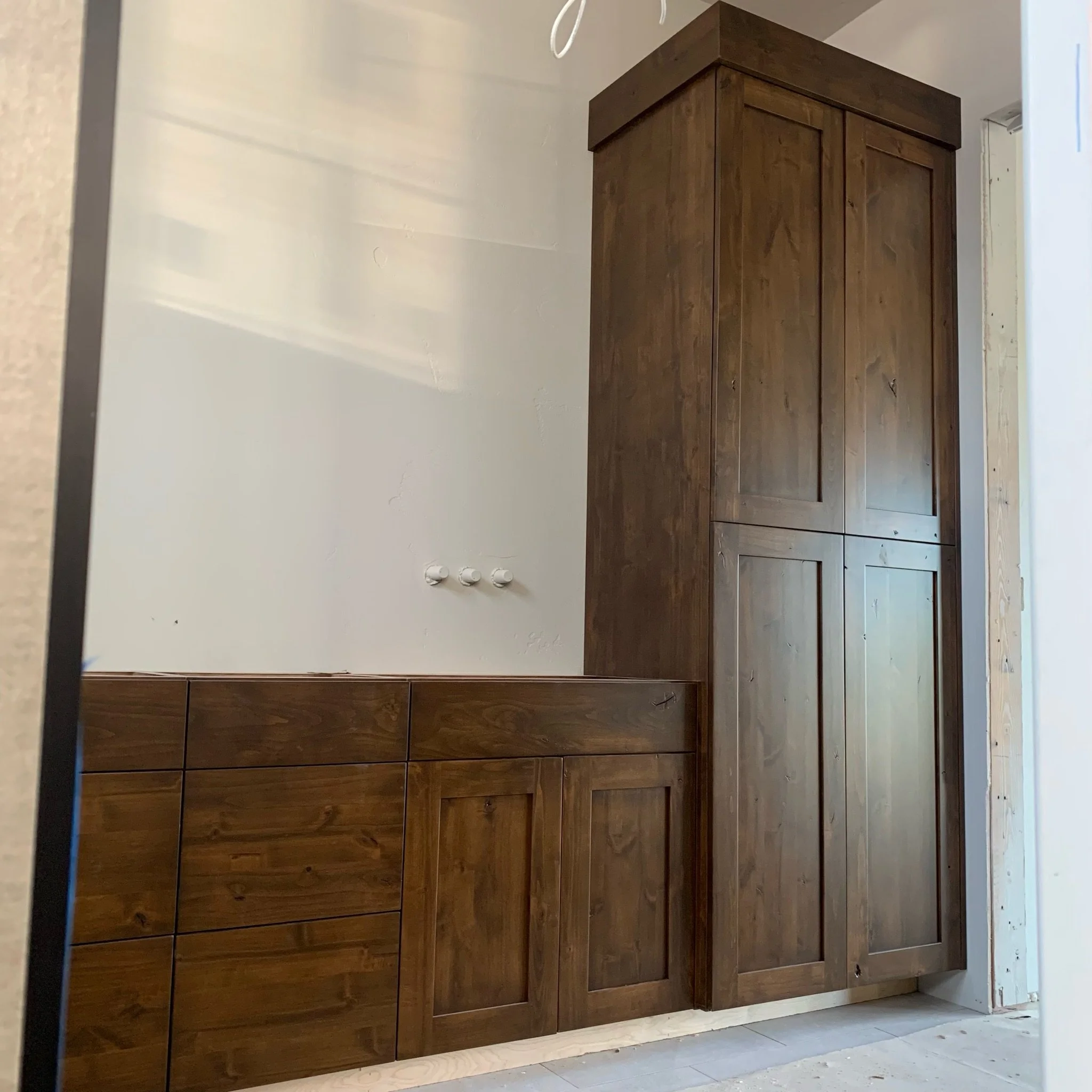 A wooden cabinet with a dark brown finish positioned against a plain beige wall. The cabinet appears to have multiple compartments or drawers. The setting suggests an indoor area, possibly a room under renovation.
