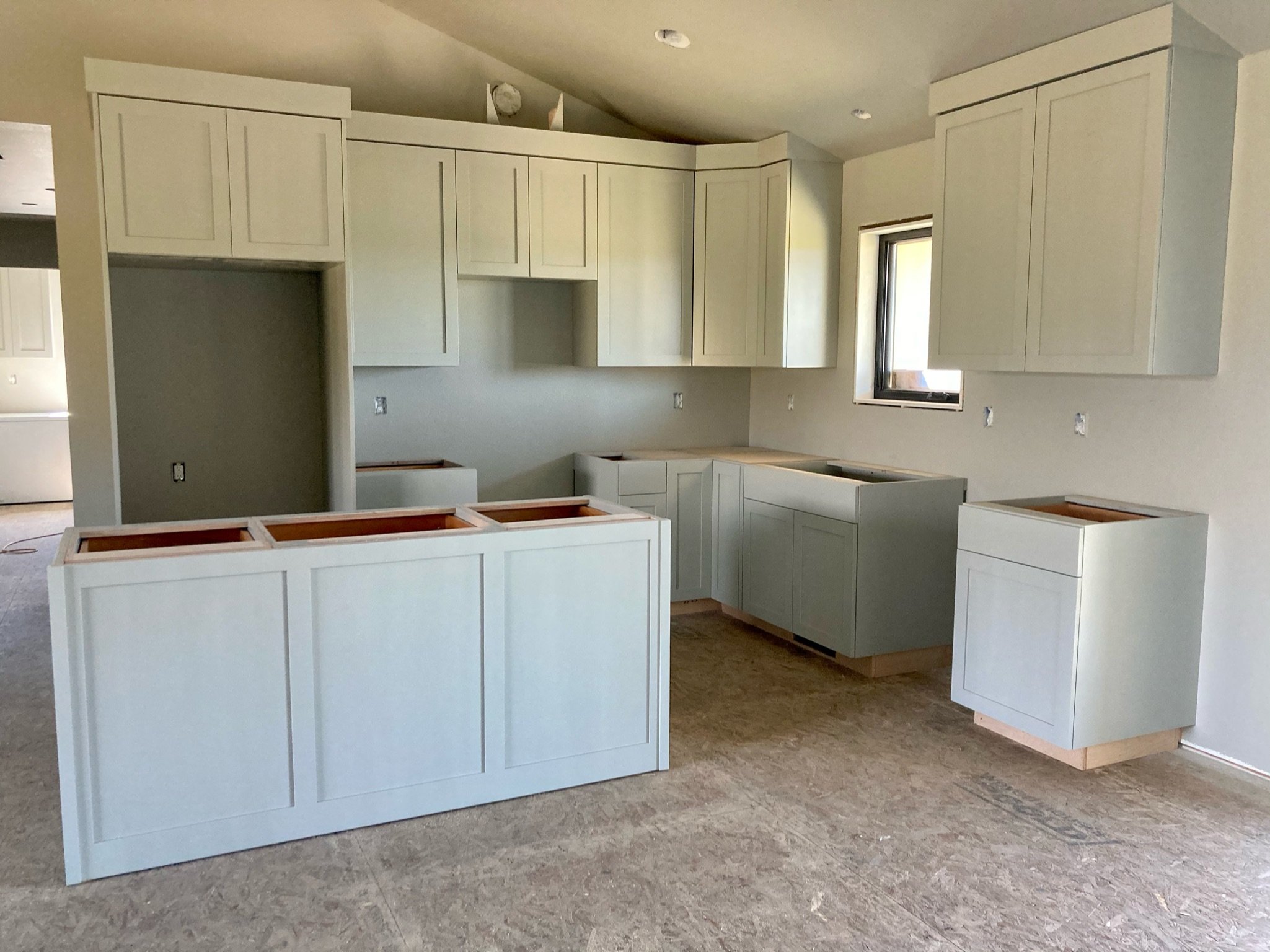 Unfinished kitchen with white cabinets and countertops, no appliances, and a window on the right side.