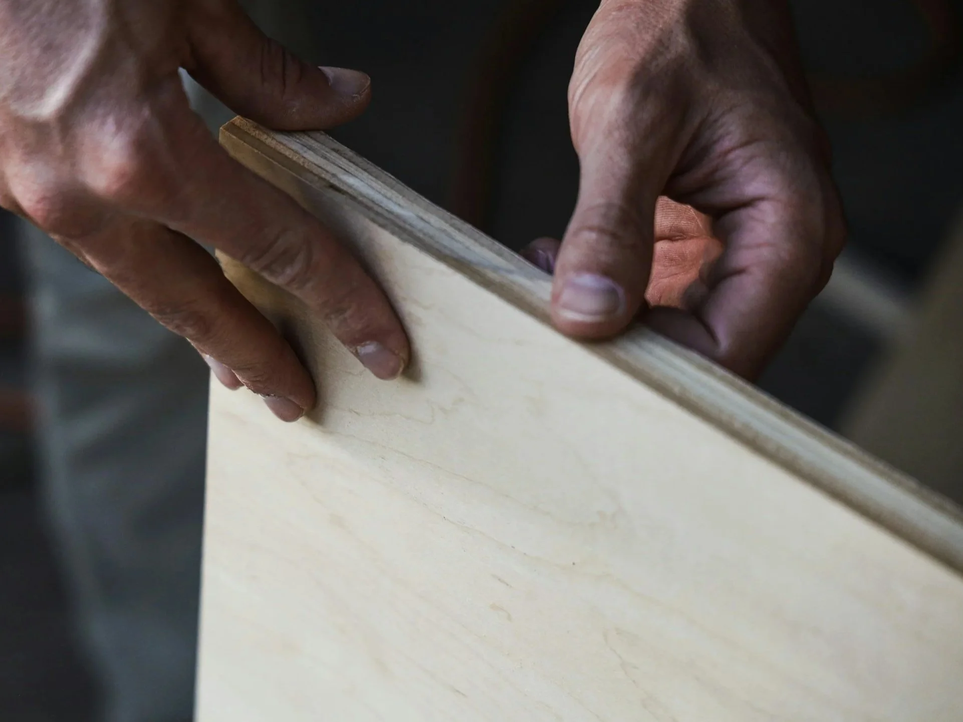Close-up of hands holding and sanding a piece of wood in a woodworking shop.
