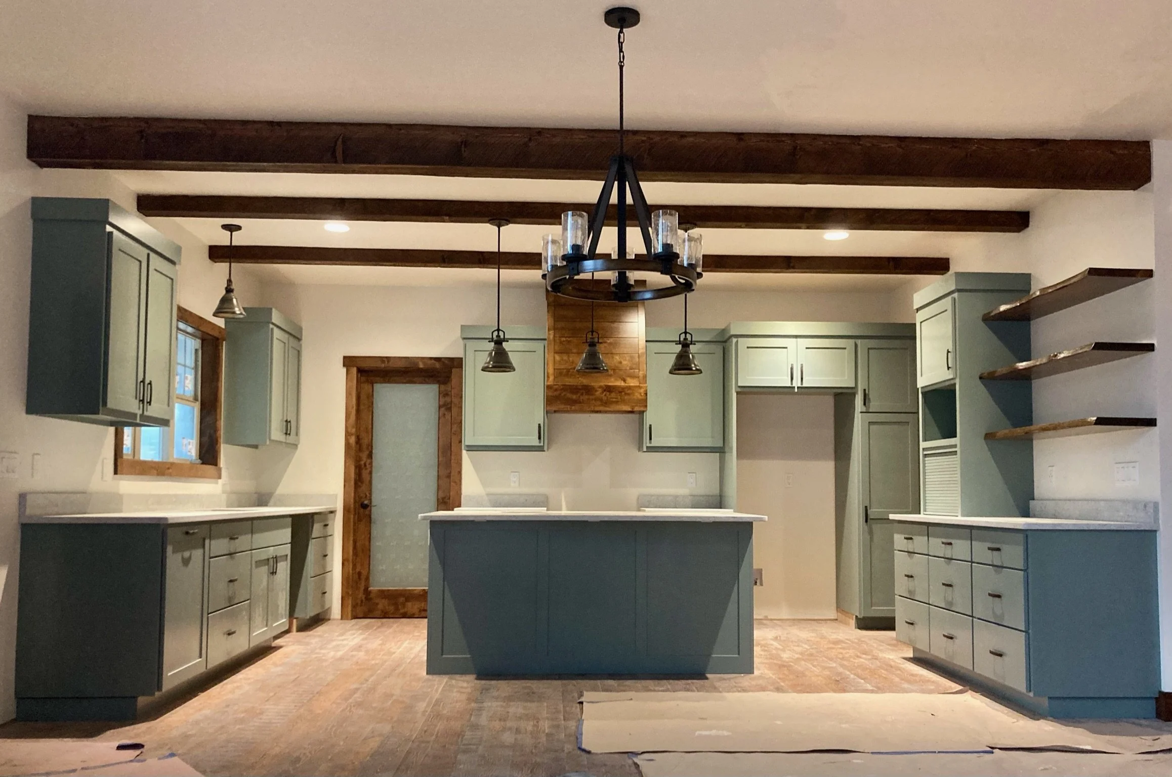 Kitchen with painted cabinets, wooden beams on ceiling, central island, and chandelier.