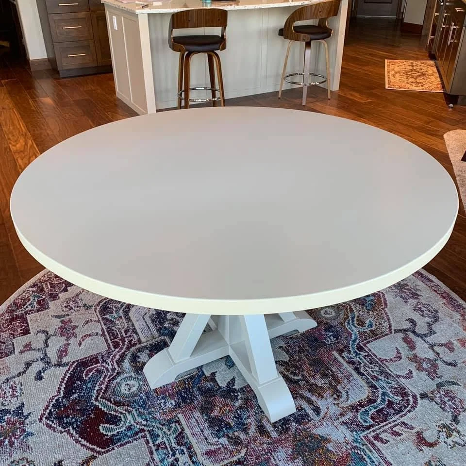 A round, white dining table on a patterned area rug in a kitchen with wooden floors and bar stools in the background.