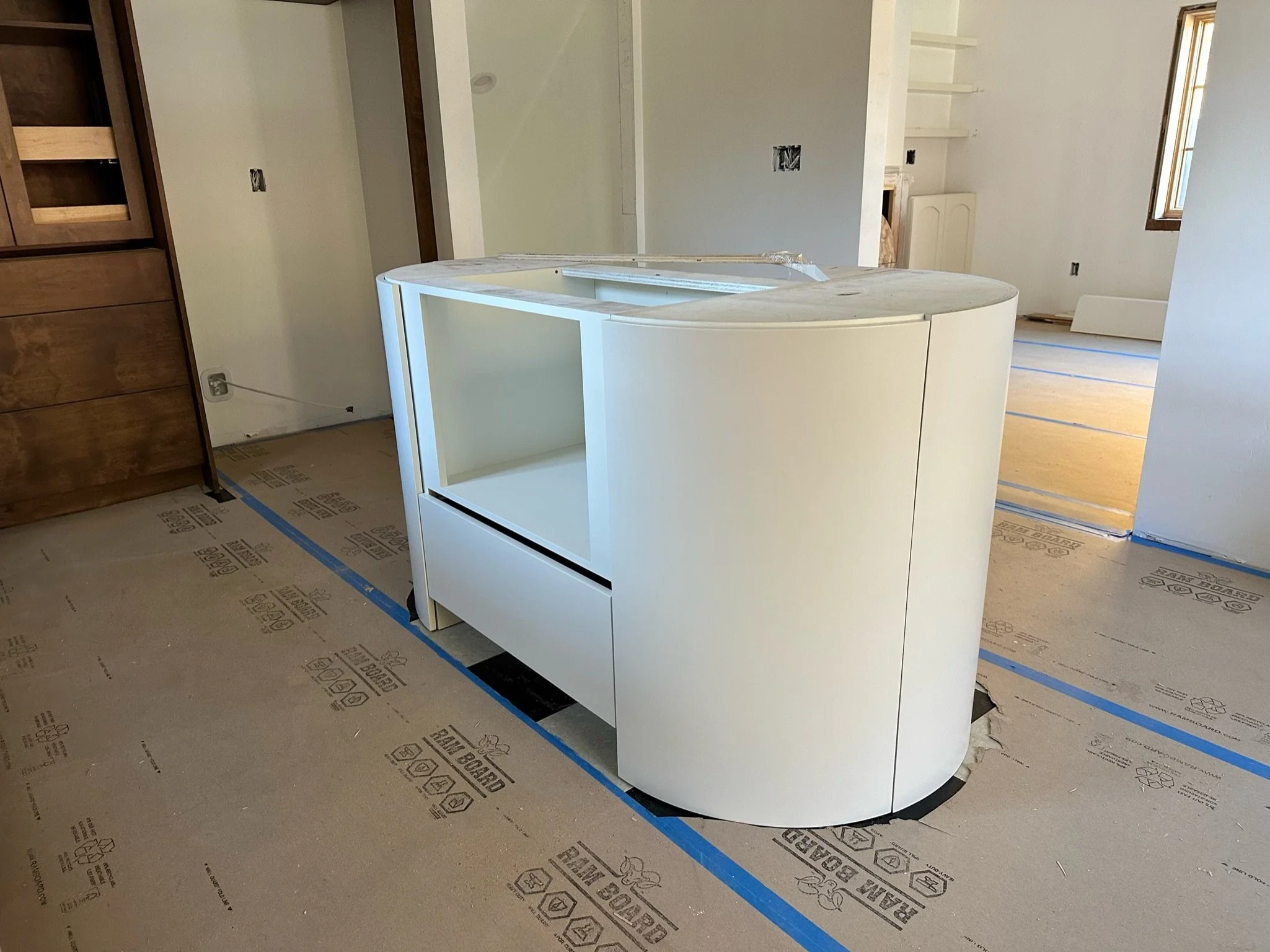 Kitchen in progress with white cabinetry, open shelves, and unfinished walls. Protective floor covering and construction materials visible.