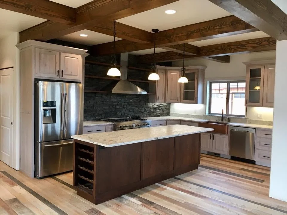 Modern kitchen with stainless steel refrigerator, island with granite countertop, wooden cabinets, black stone backsplash, and pendant lighting.
