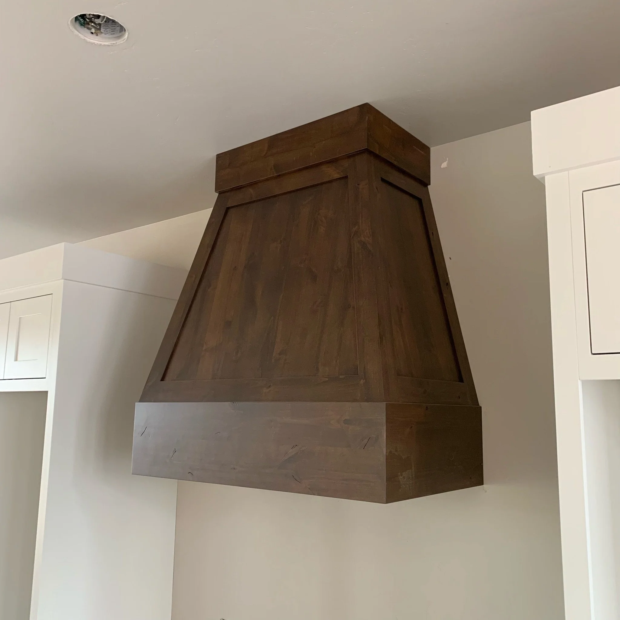 Ceiling with an oval-shaped hole showing electrical wiring, and a corner of a wooden cabinet or feature wall in the room.