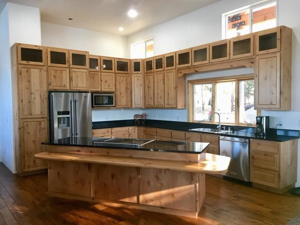 Kitchen with wooden cabinets, black countertop, stainless steel refrigerator, microwave, dishwasher, and a breakfast bar, with a window overlooking an outdoor scene.