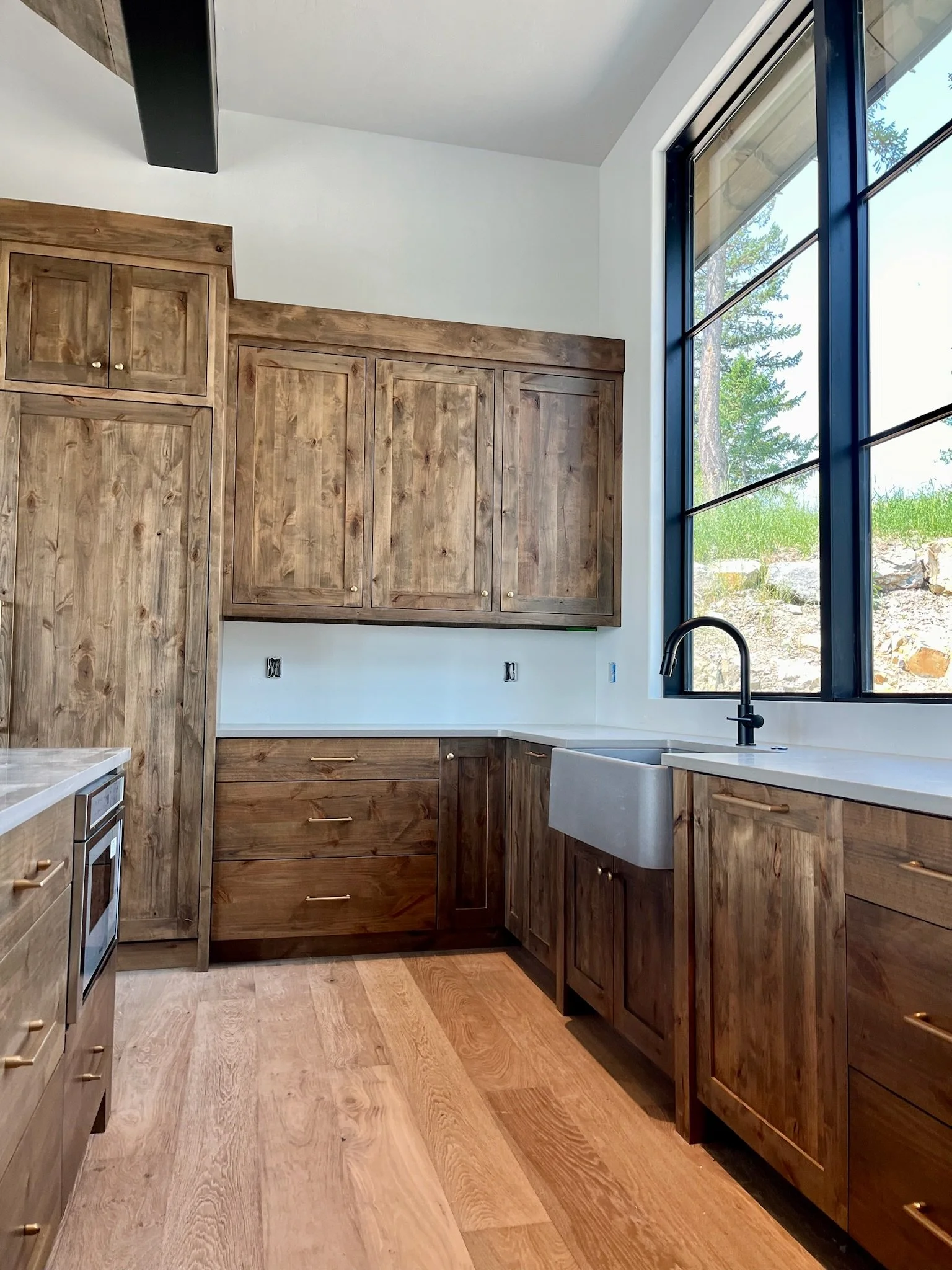 Kitchen with wooden cabinets, a large window, a farmhouse sink, and a view of trees outside.