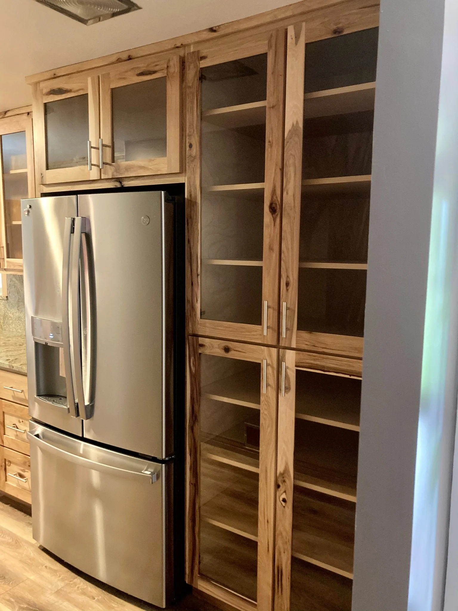 A kitchen with a stainless steel refrigerator and a wooden cabinet with glass doors and open shelves.