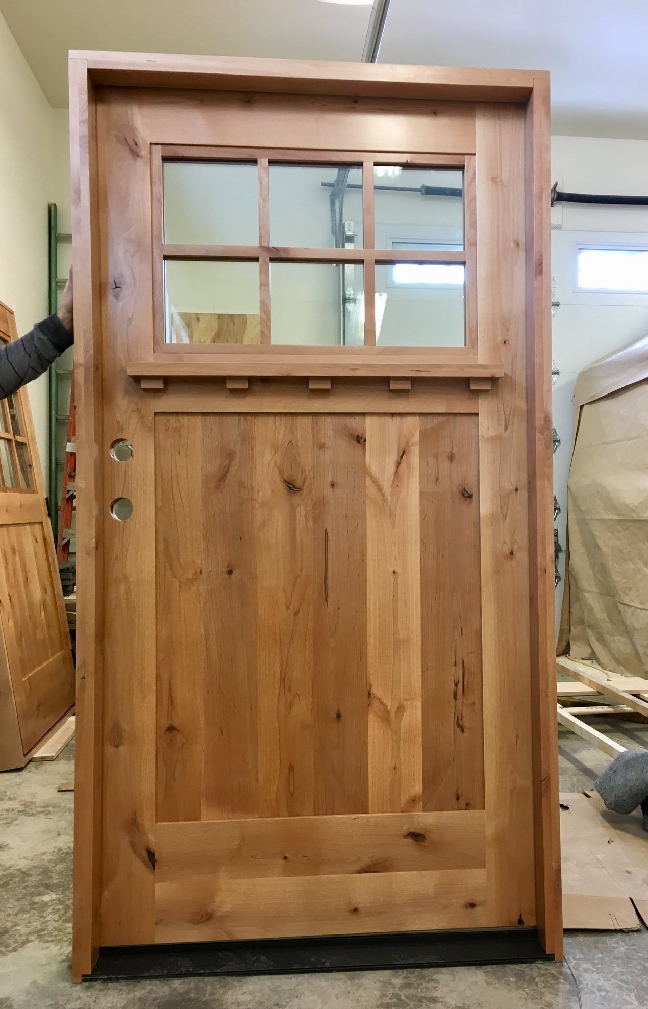 A wooden door with a glass window at the top, consisting of six panes, and a lower solid wood panel. The door is in a workshop or construction area.