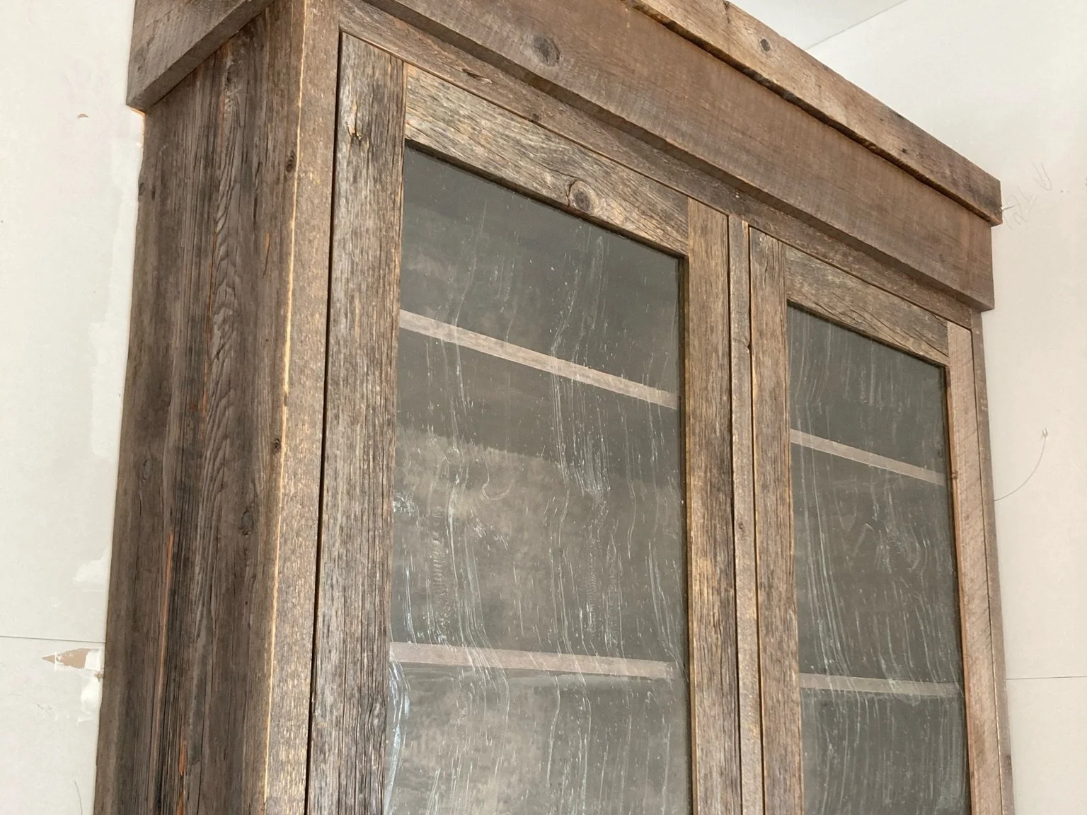 A wooden cabinet with glass doors and shelves inside, against a white wall.