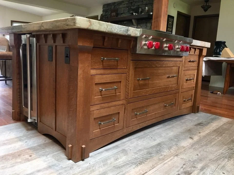Wooden kitchen island with a marble countertop and red knobs, featuring multiple drawers and cabinets.