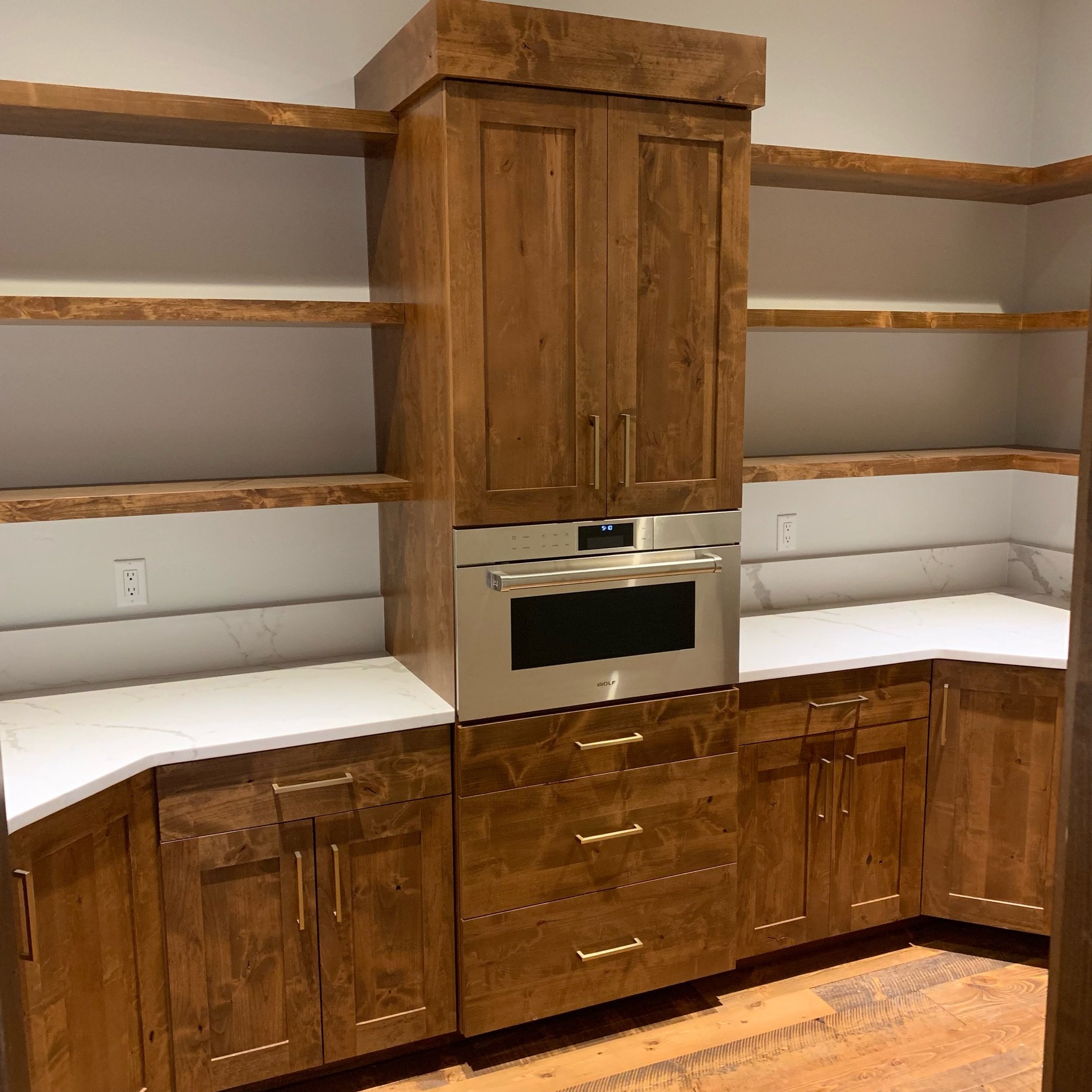A kitchen with wooden cabinets and open shelving, a built-in oven, and a white countertop. The cabinets are made of polished wood with a natural finish.