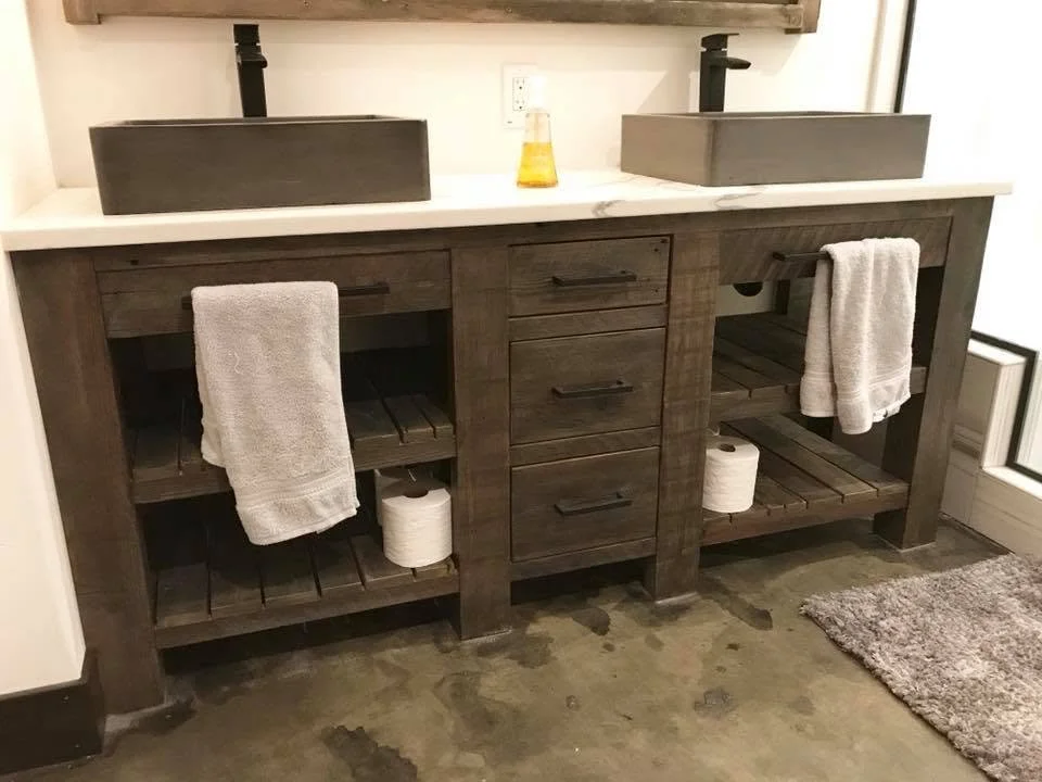 Double vanity bathroom with dark wood finish, two vessel sinks, towels hanging on either side, and two rolls of toilet paper underneath.
