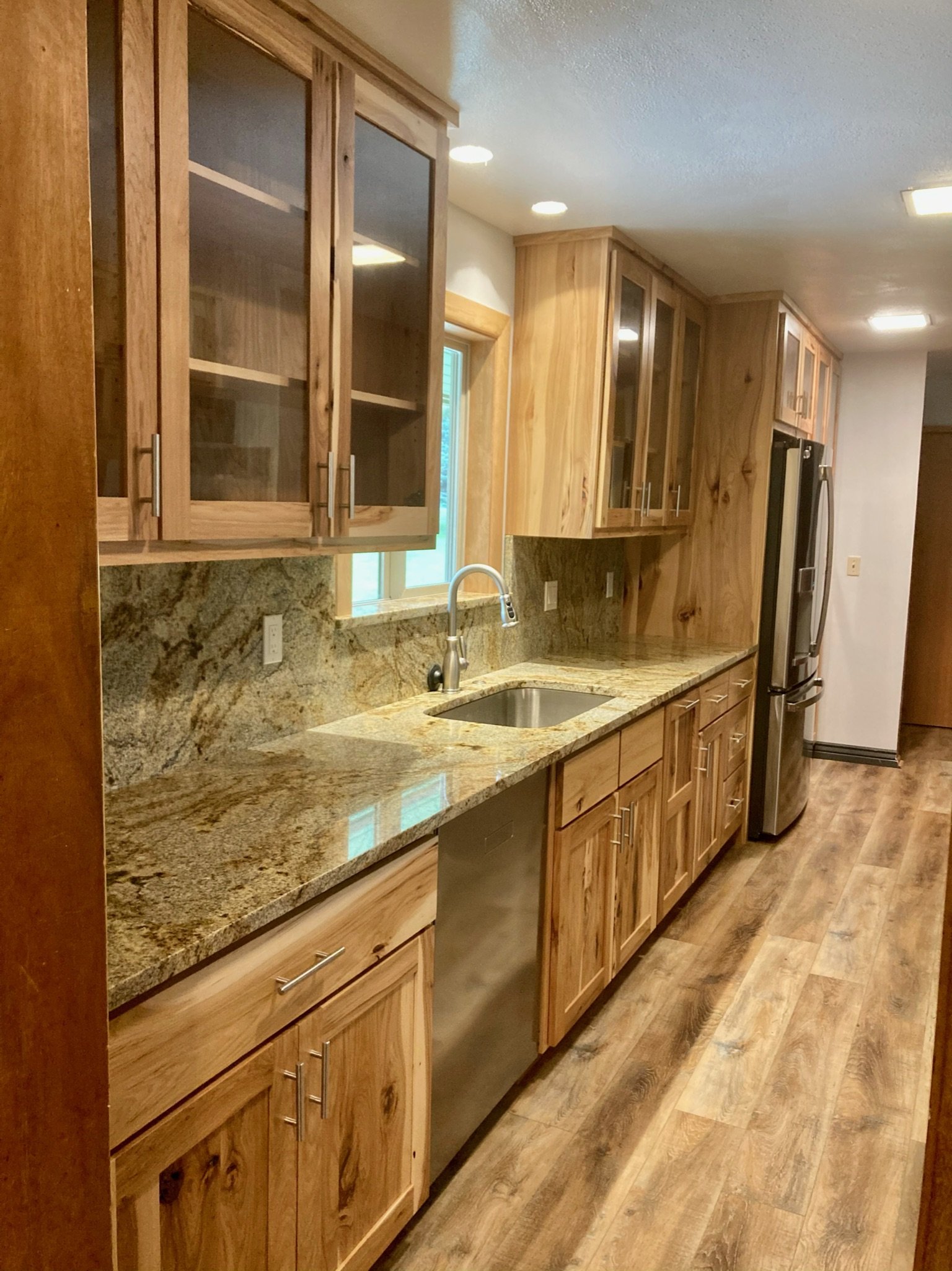 Kitchen with wooden cabinets, granite countertops, stainless steel sink, and hardwood flooring.