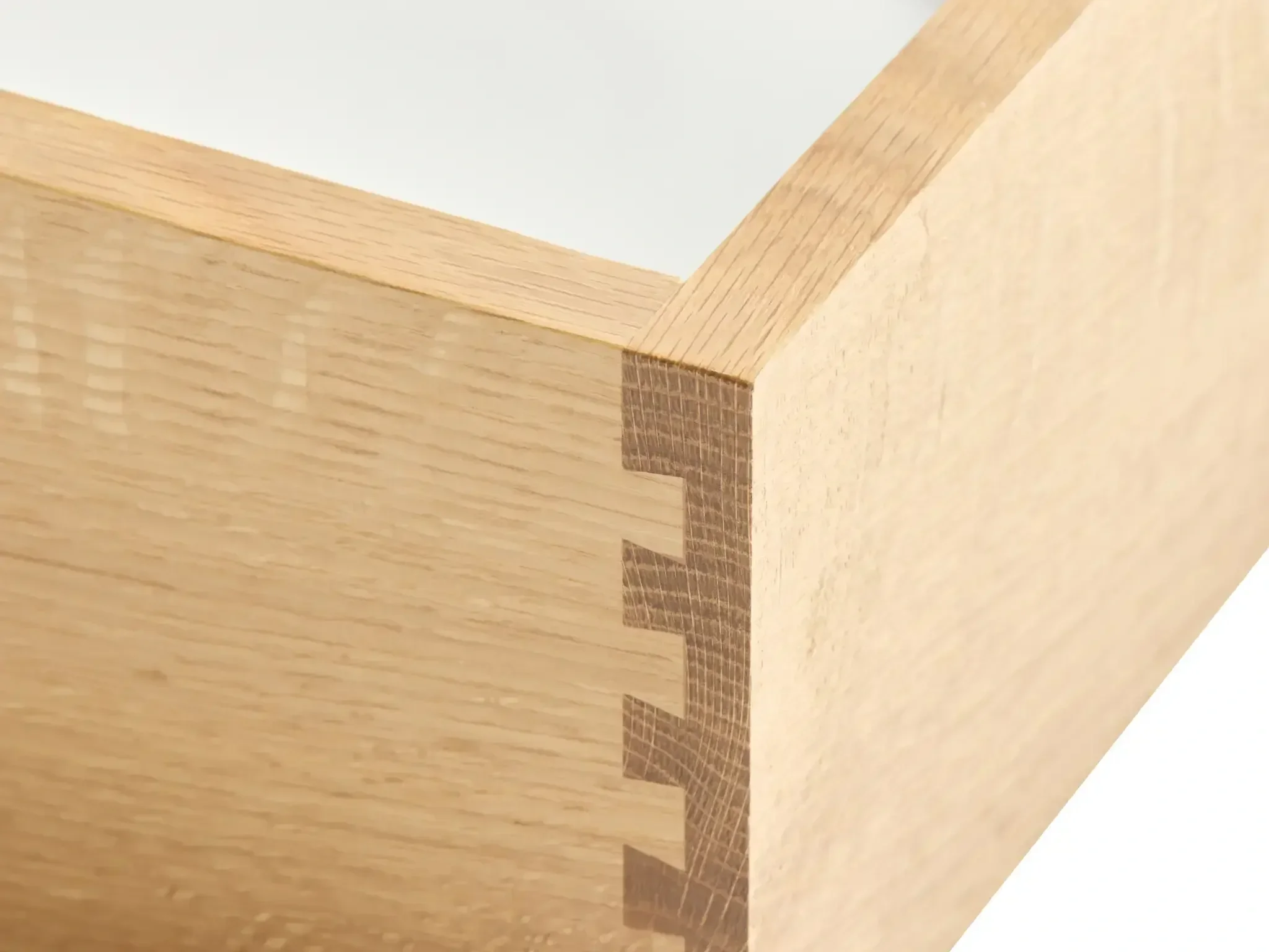 Close-up view of the corner of a wooden object with a light-colored wood finish, showing detailed wood grain and a beveled edge.