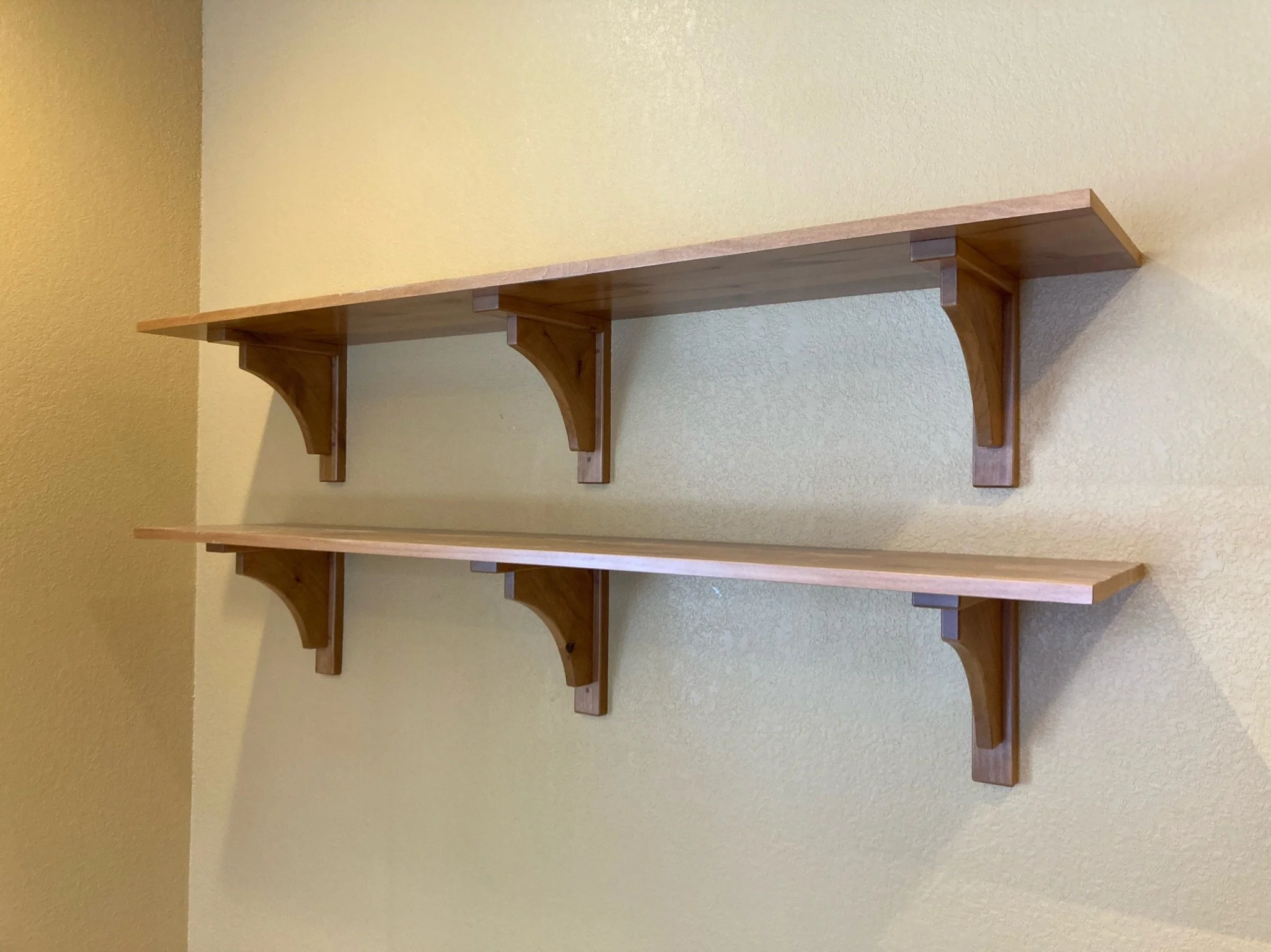 A wooden wall shelf mounted on a yellow wall with brackets.