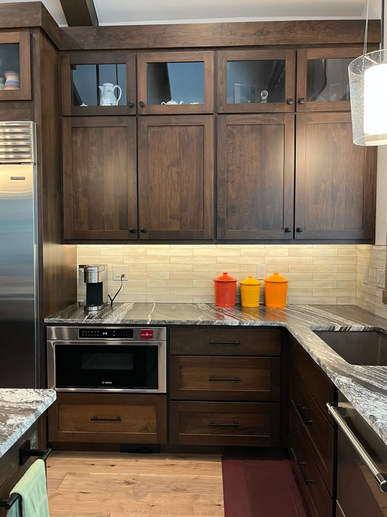 Kitchen with dark wooden cabinets, a stainless steel oven, granite countertops, a coffee maker, and three colorful canisters on the counter.