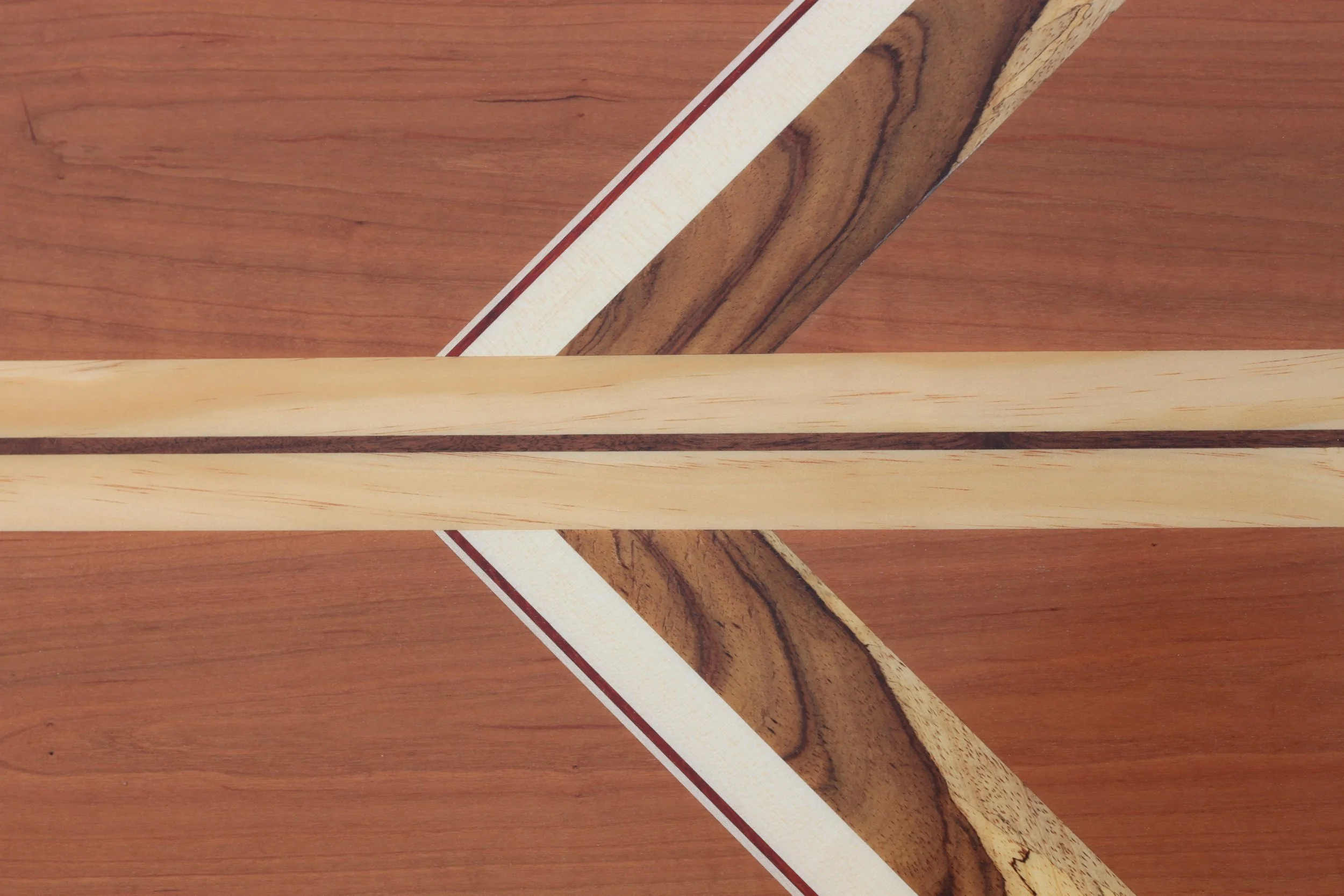 Close-up of a wooden table with various pieces of wood arranged on it, including a long light-colored wooden strip, a darker piece of wood with a natural grain, and a curved wooden piece with a dark edge.