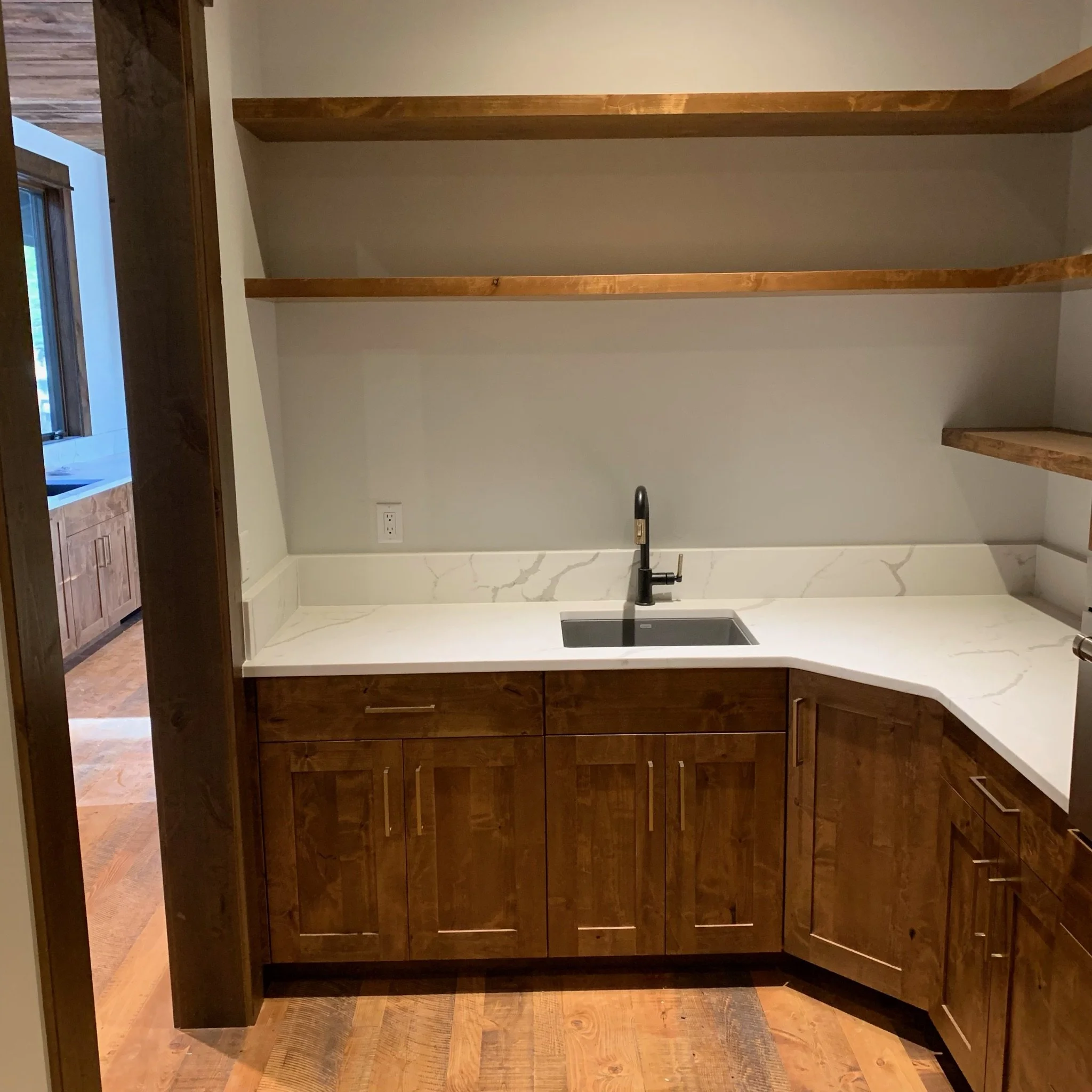 Empty kitchen with wooden cabinets and a white countertop, black faucet, and a marble backsplash.