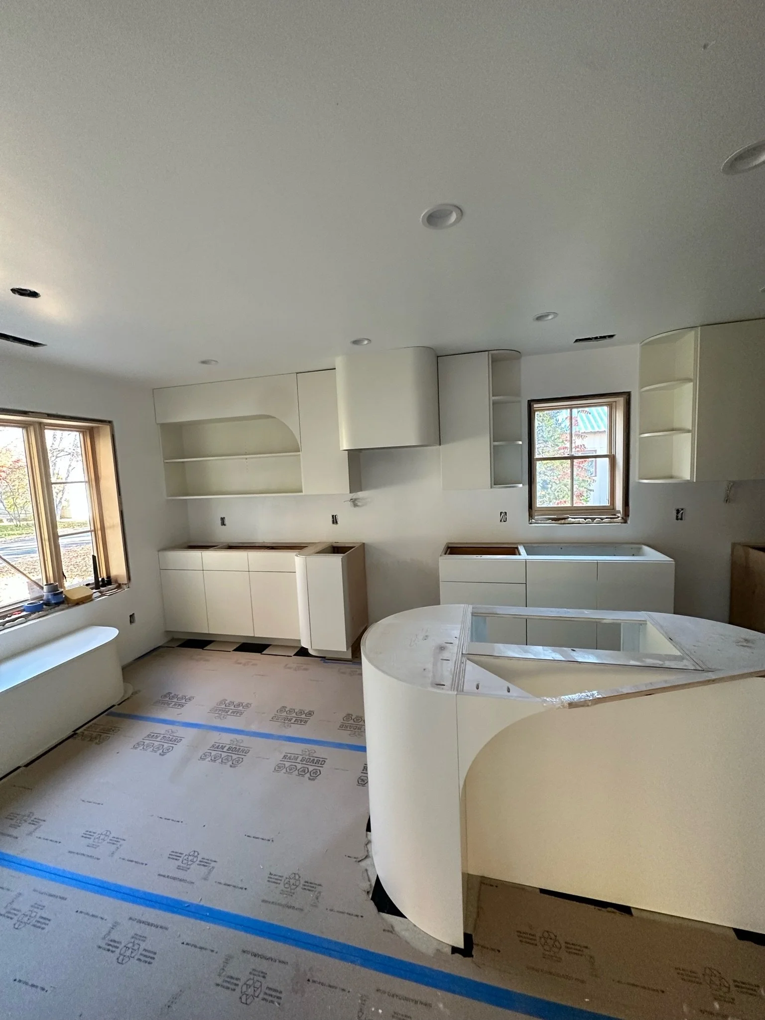 Newly constructed kitchen with white cabinets, large windows, and a circular kitchen island under development.