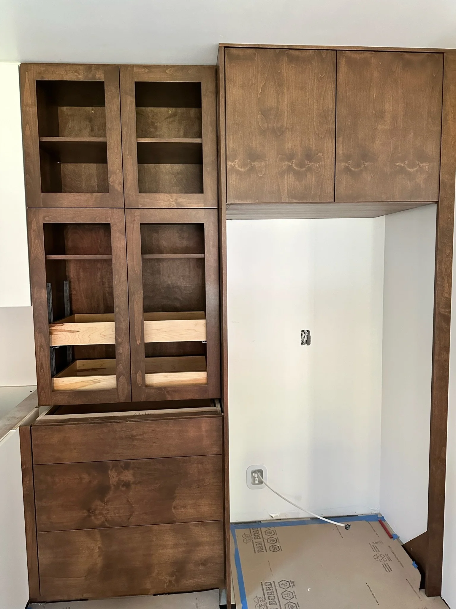 Partially built wooden cabinet and shelves against a white wall with an electrical outlet and cords at the bottom.