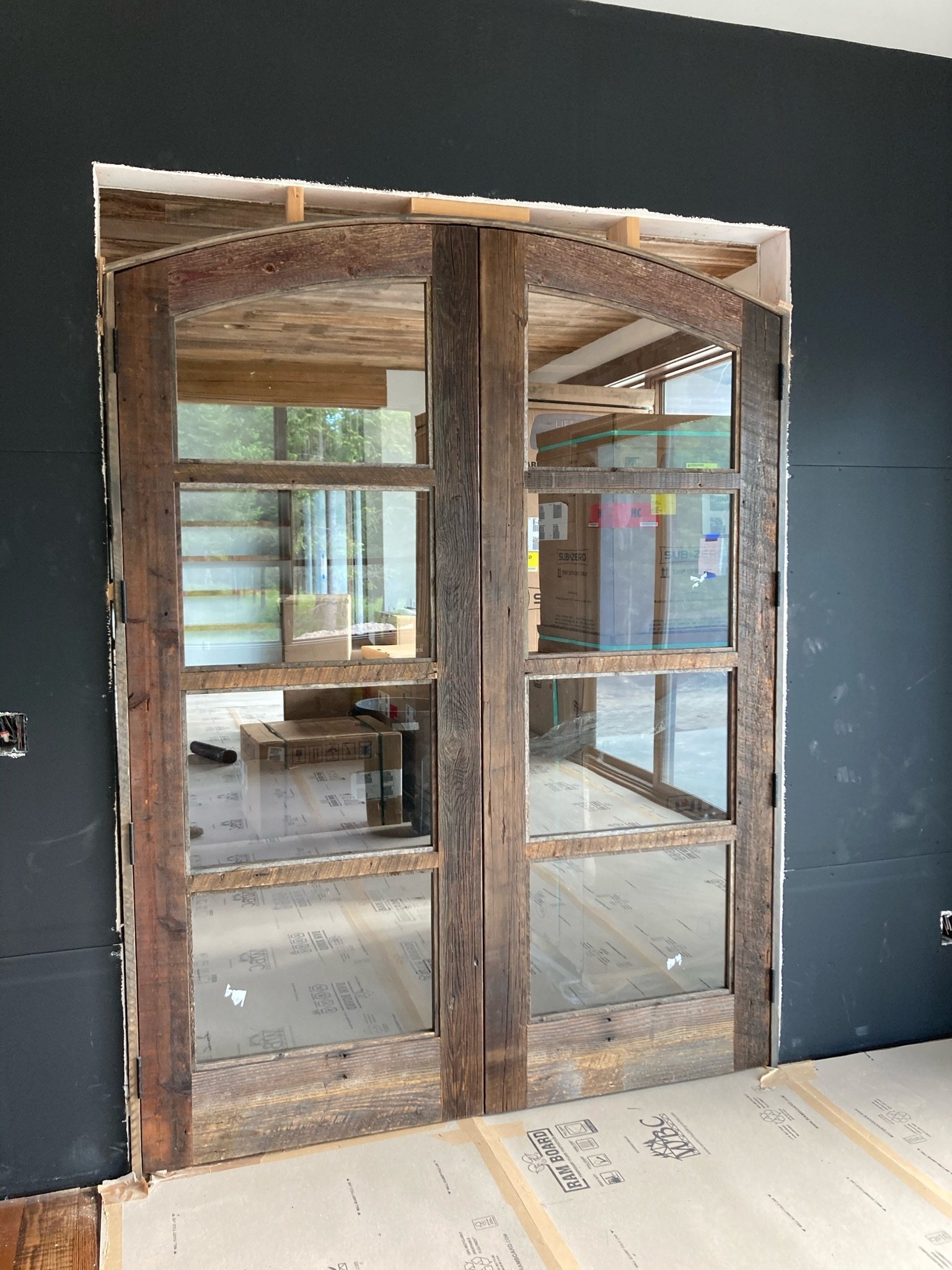 A rustic wooden door with glass panels, currently installed in a wall under construction, with visible tools and boxes inside the building.