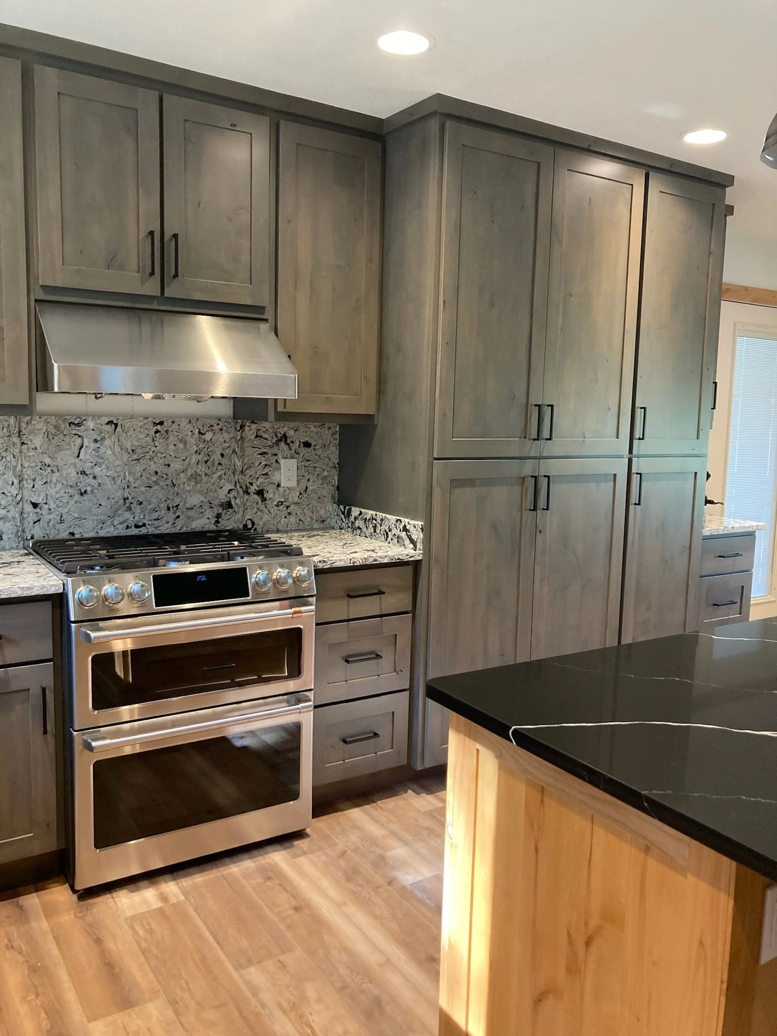 Kitchen with wooden cabinets, granite countertops, stainless steel oven and stove, and wood flooring.