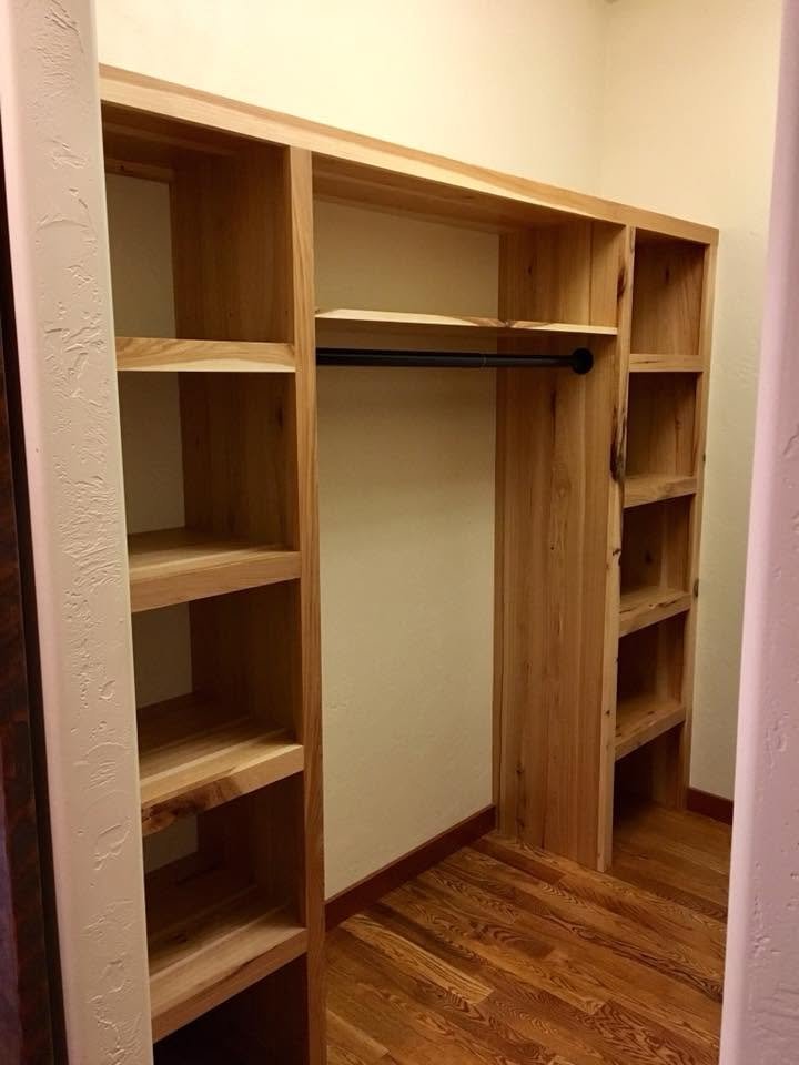 Empty wooden closet with shelves and a hanging rod in a room with hardwood floor.