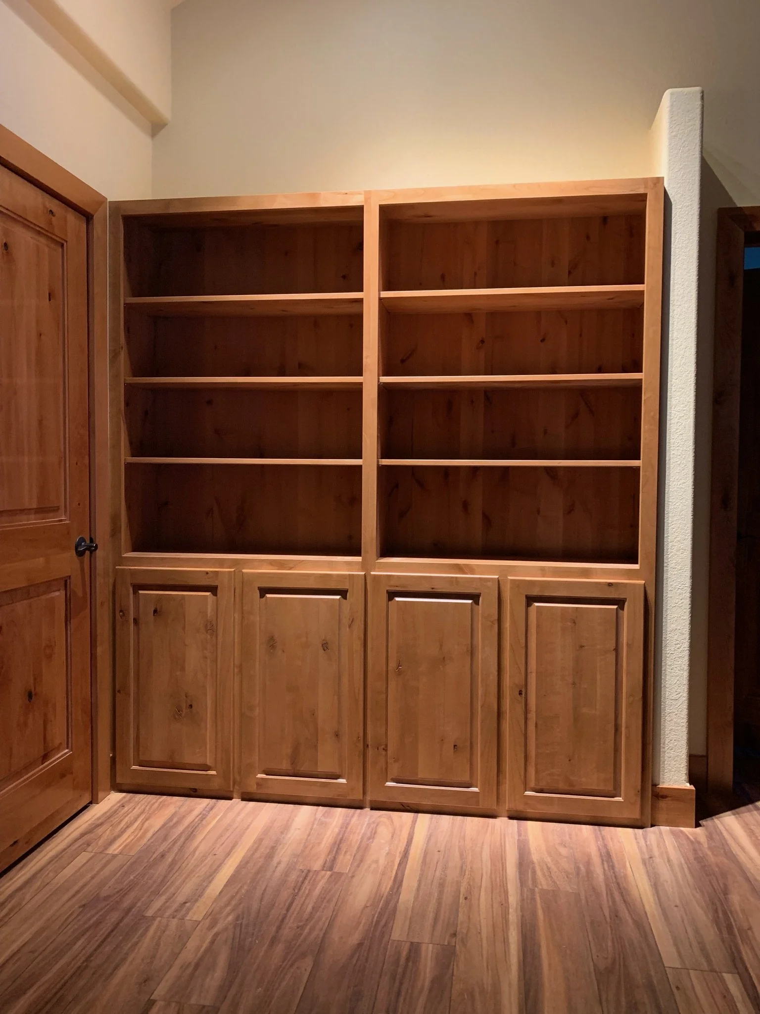 Empty wooden bookshelf against a cream-colored wall in a room with wood flooring.