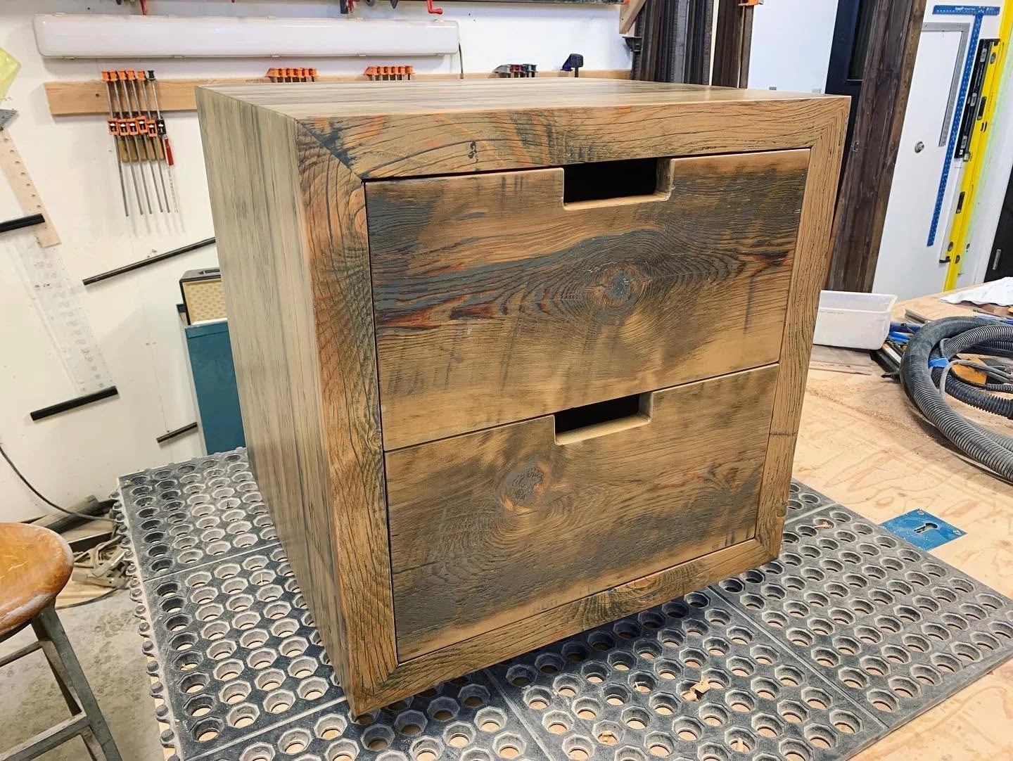 A wooden two-drawer cabinet with cut-out handles in a woodworking workshop.