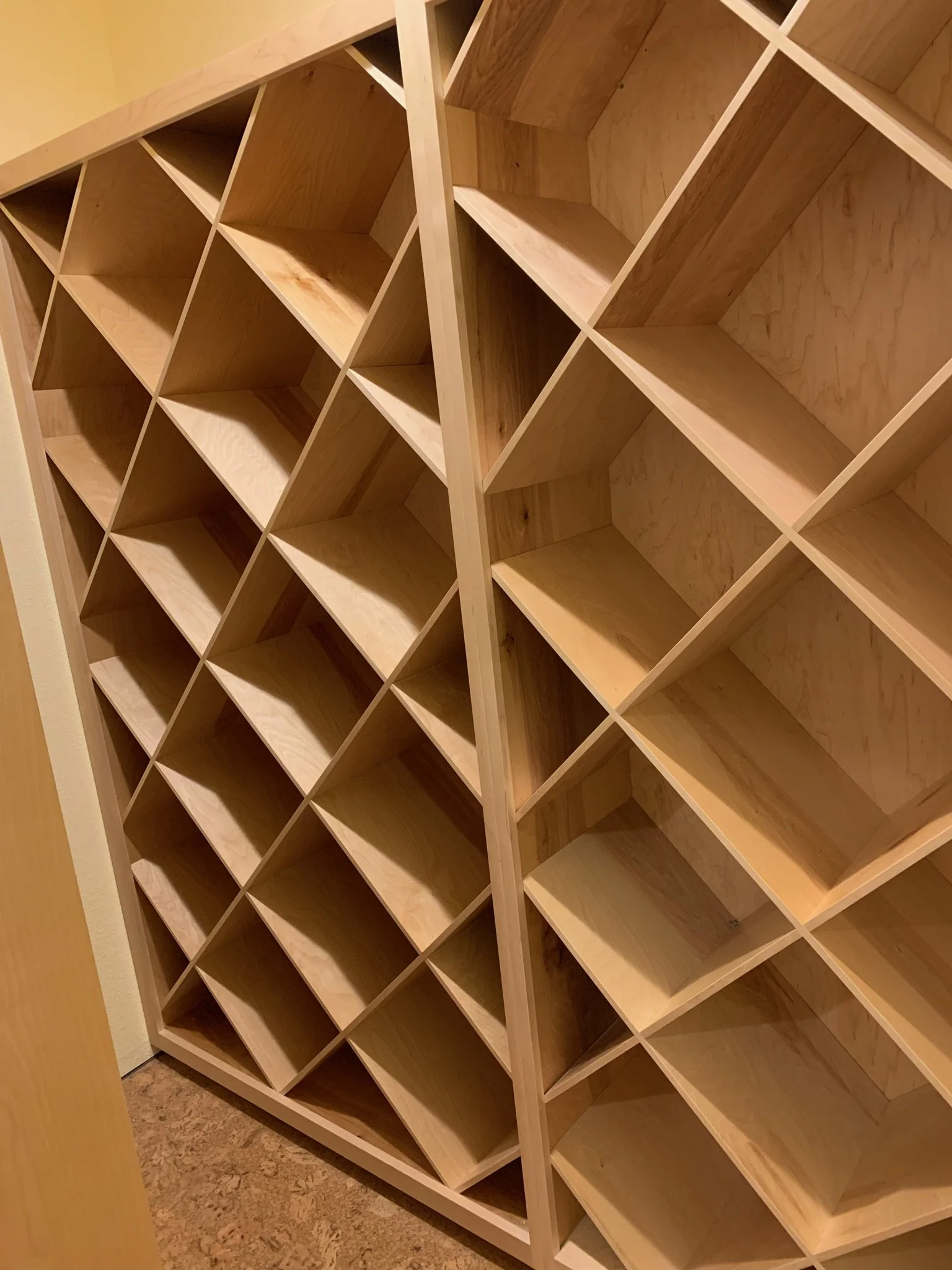 Empty wooden cubby-style shelves arranged in a grid pattern against a beige wall.