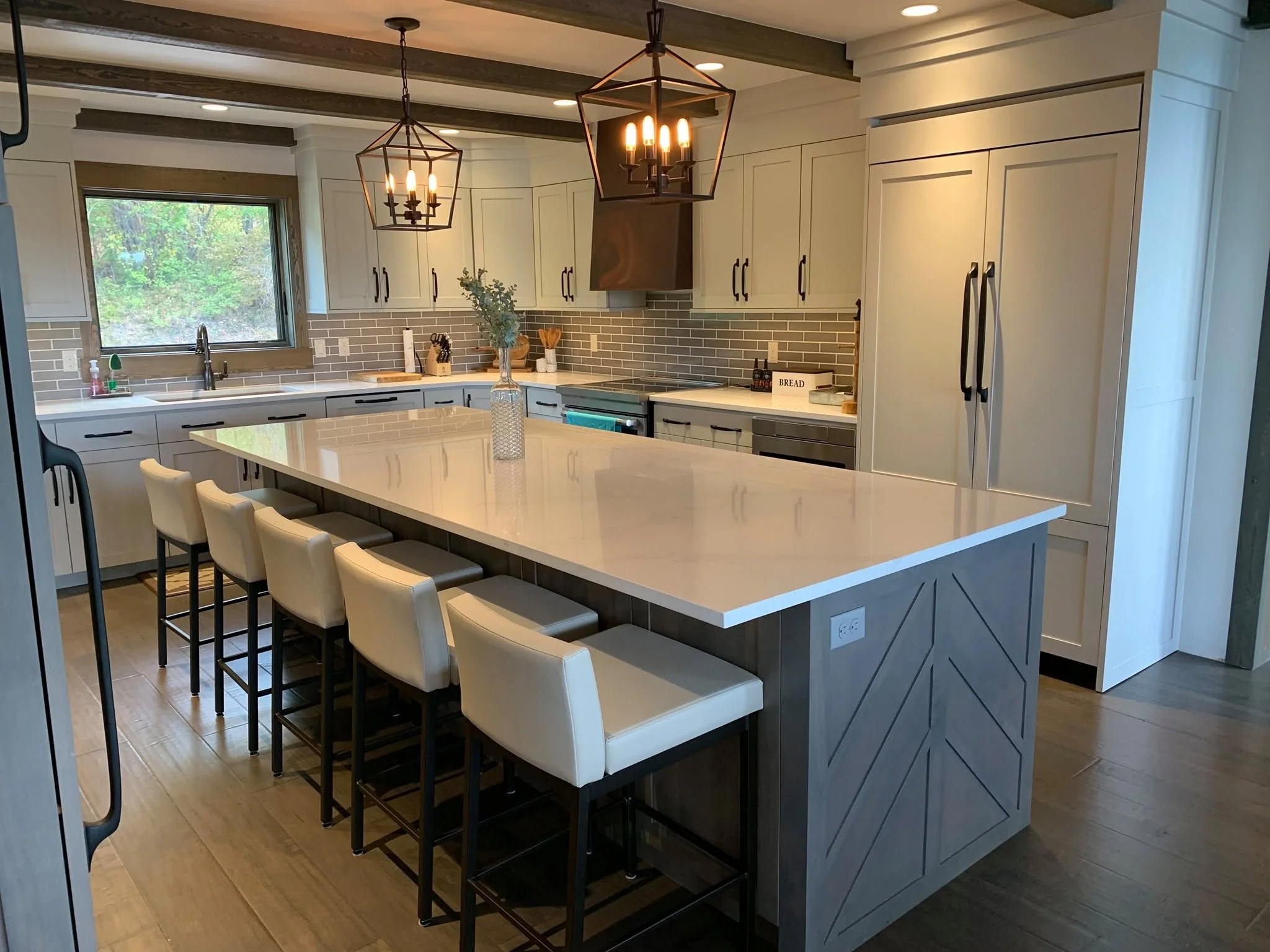 Modern kitchen with white cabinets, a large island with white countertop, beige bar stools, and pendant lighting fixtures