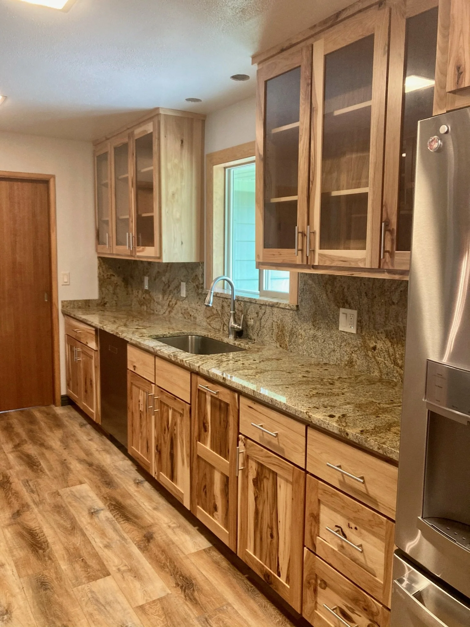 Kitchen with wooden cabinets, granite countertops, a sink, a window, and a stainless steel refrigerator.