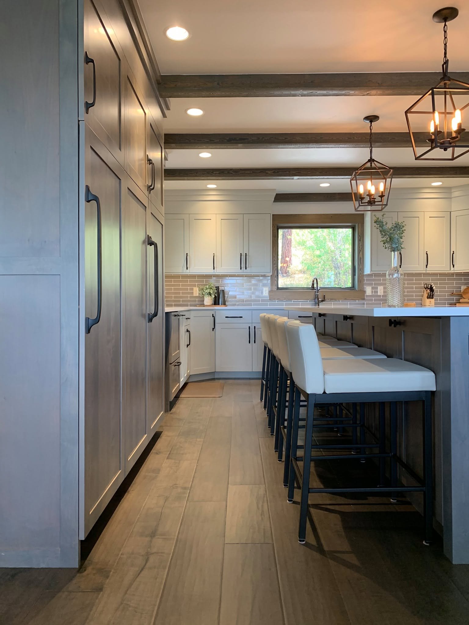 Modern kitchen with white cabinetry, a large window, and a kitchen island with white barstools, pendant lighting, and a brick backsplash.