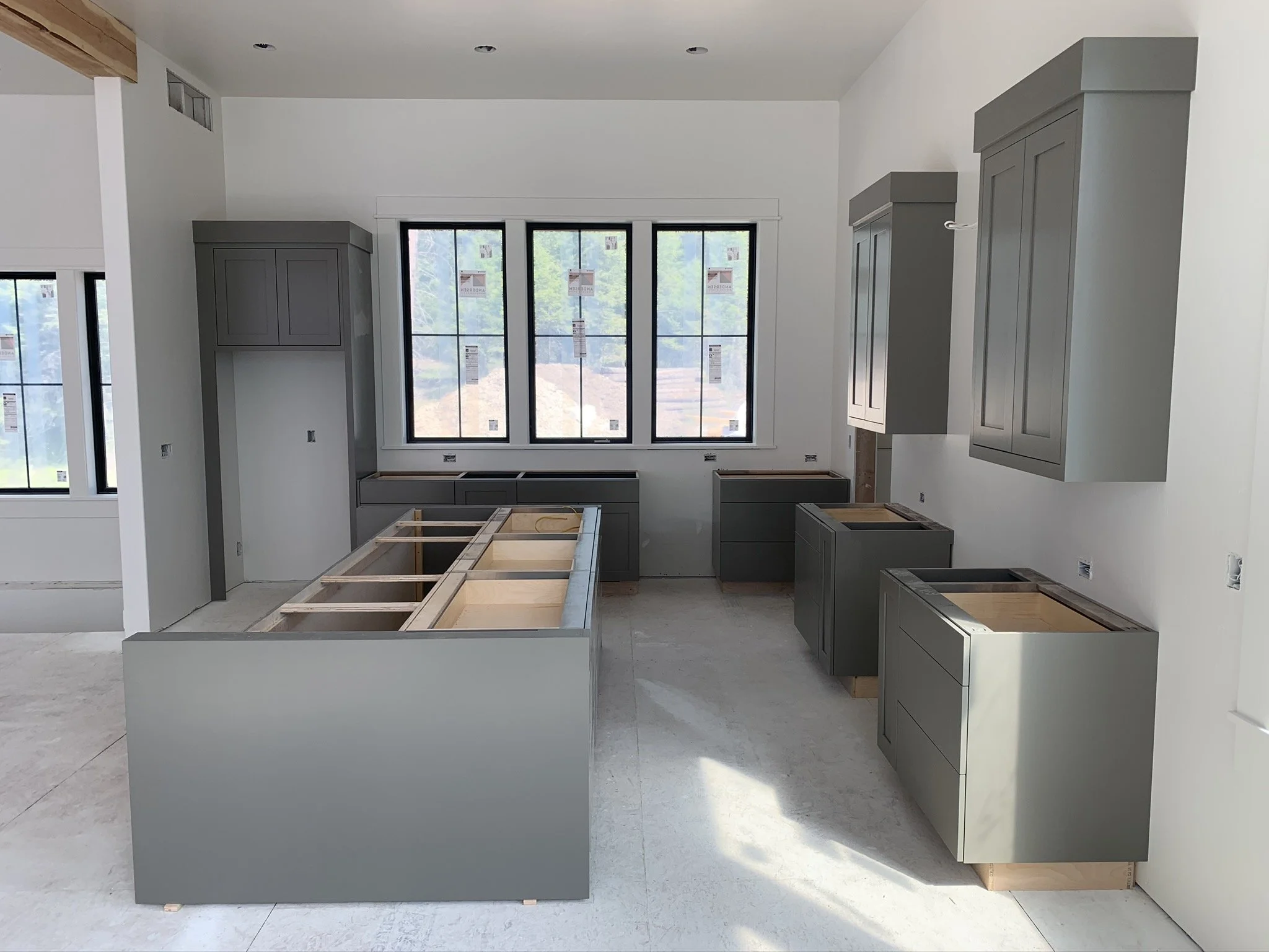 Interior of a house under construction with gray cabinets, large windows, and kitchen island framework.