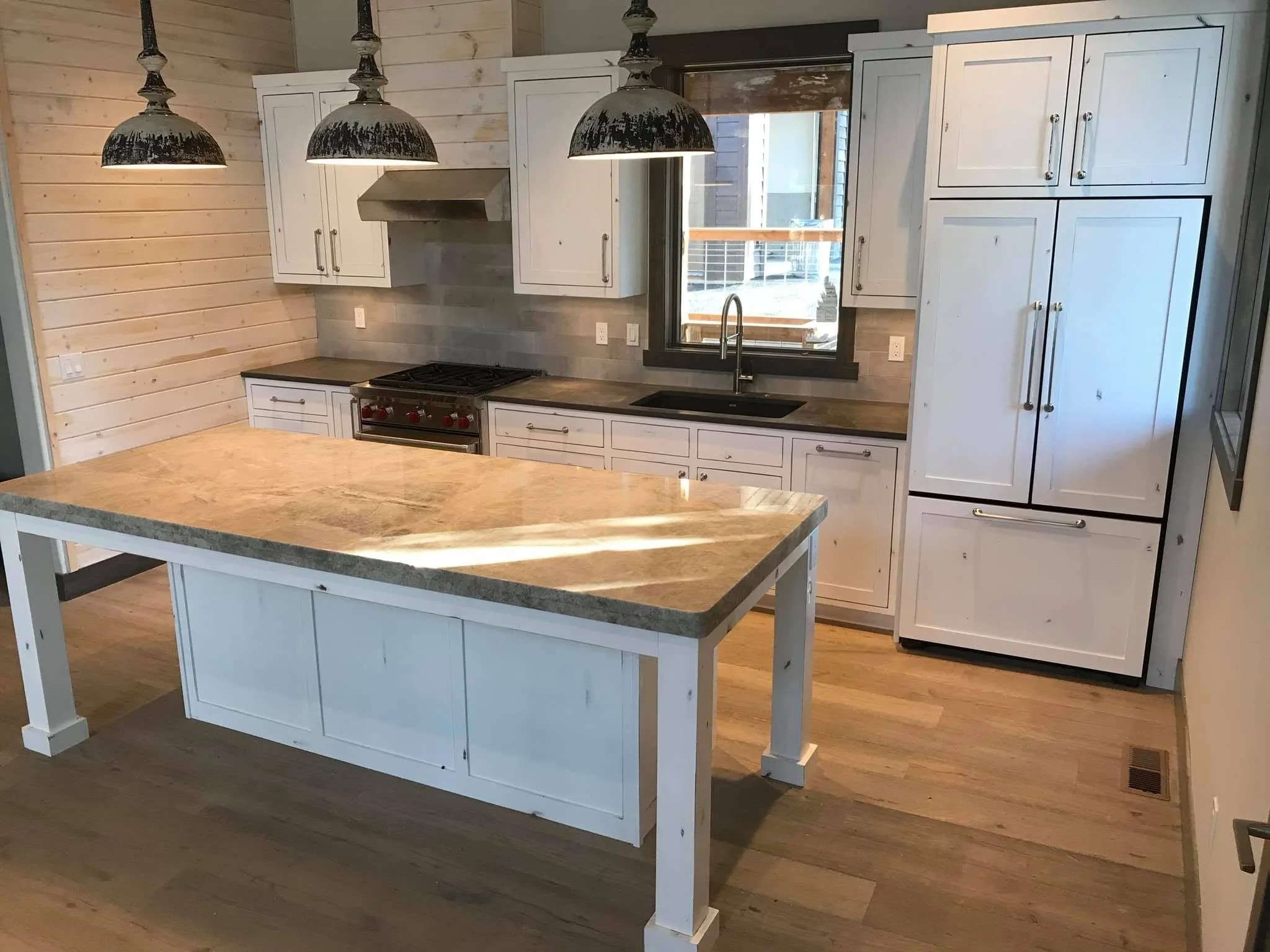 Modern kitchen with white cabinets, black countertops, a large window, a stove, and rustic black pendant lights.