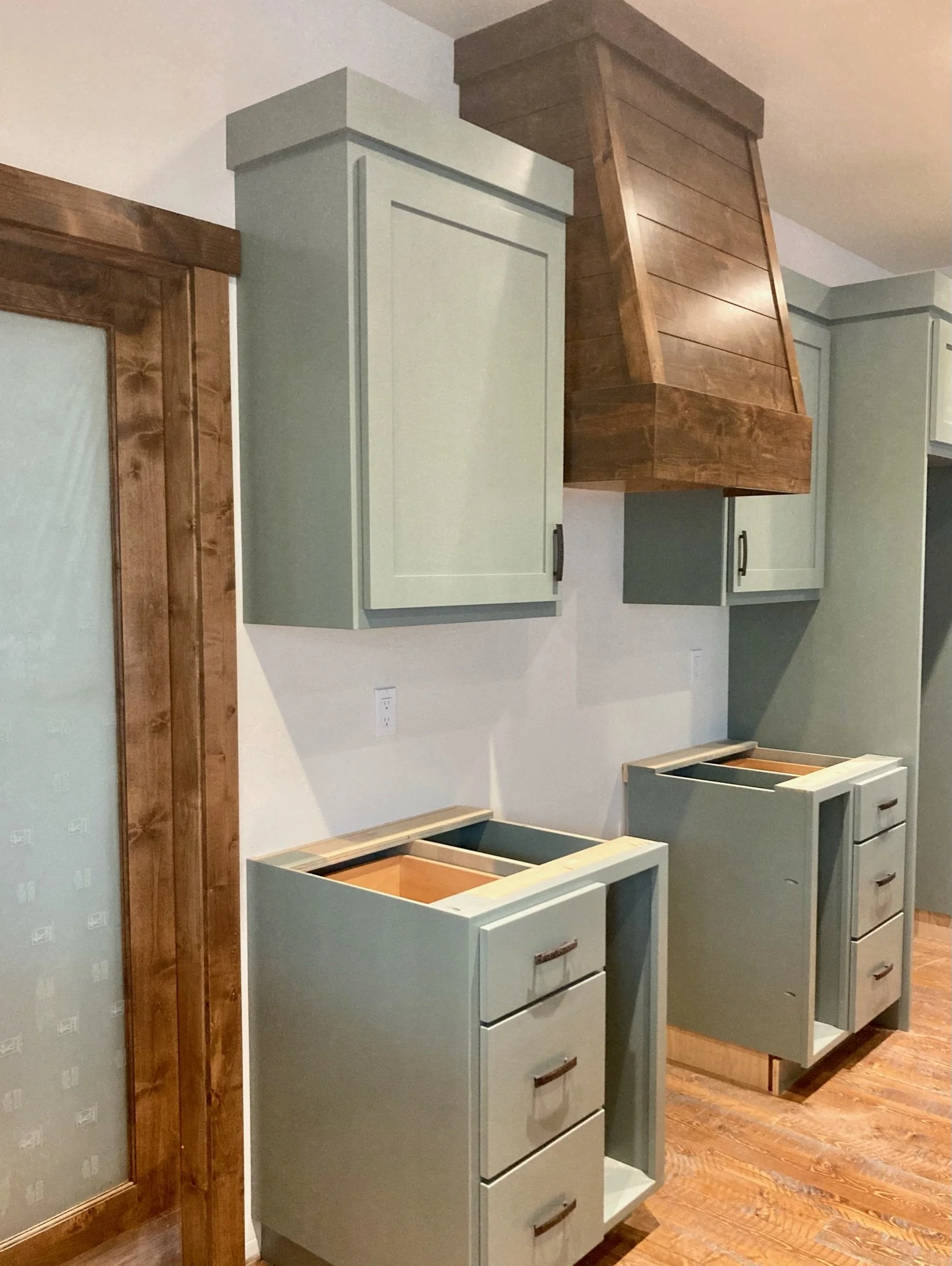 Unfinished kitchen cabinets and a range hood in a room with hardwood floors and light-colored walls.