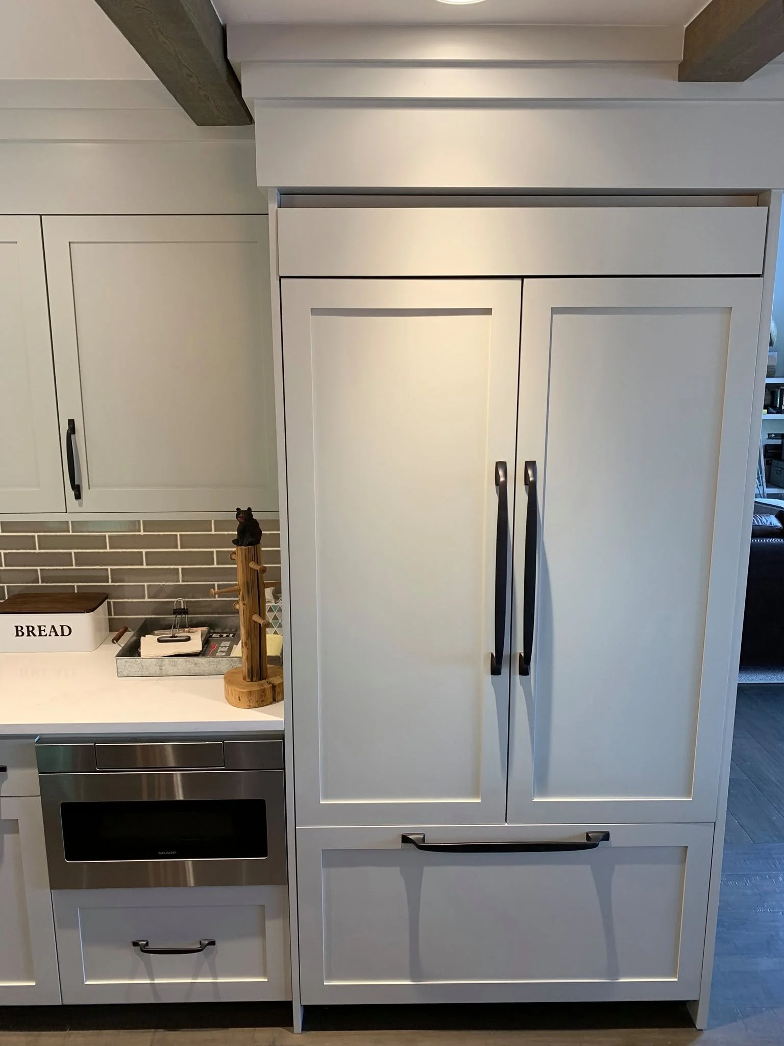 Kitchen with white cabinet, black handles, microwave, and small black cat figurine on a wooden stand.